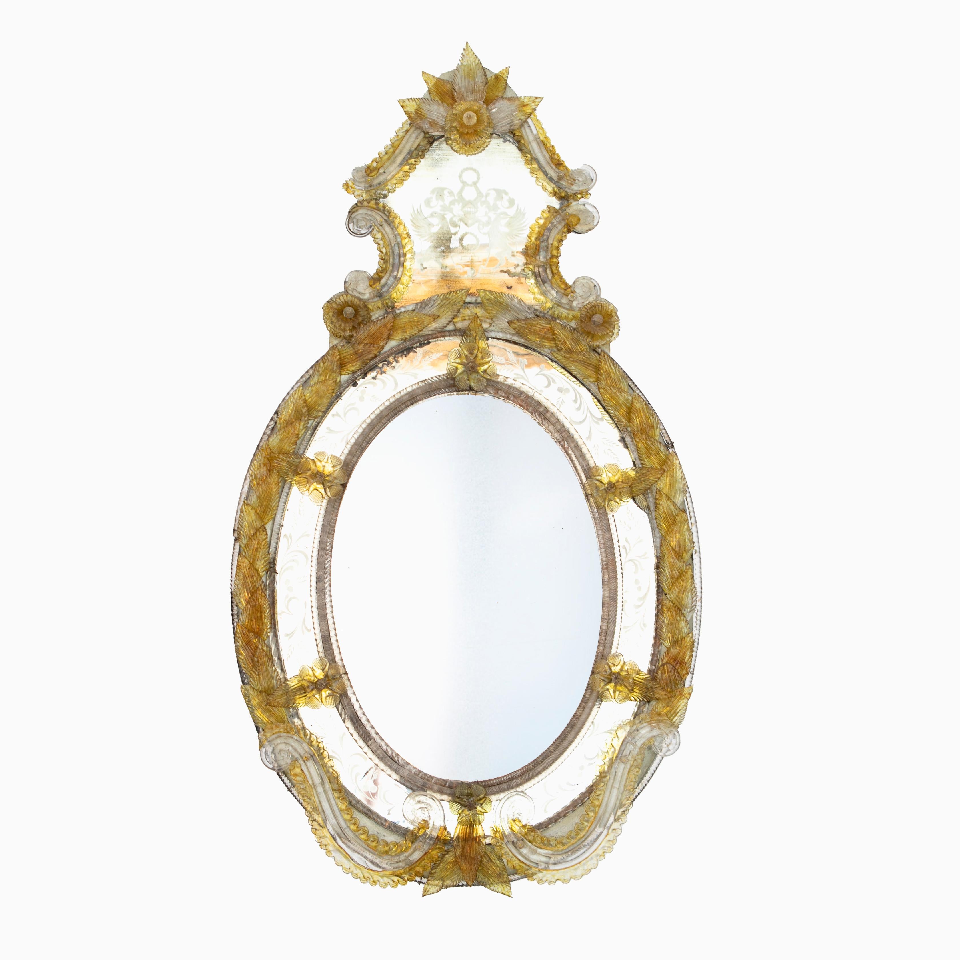 Large Italian Murano Mirror from the late 19th century featuring a yellow and clear glass molded foliate border.

Oval faceted mirror surrounded by a frame with hand engravings. At the top a mirror with an engraved badge of nobility in the form of
