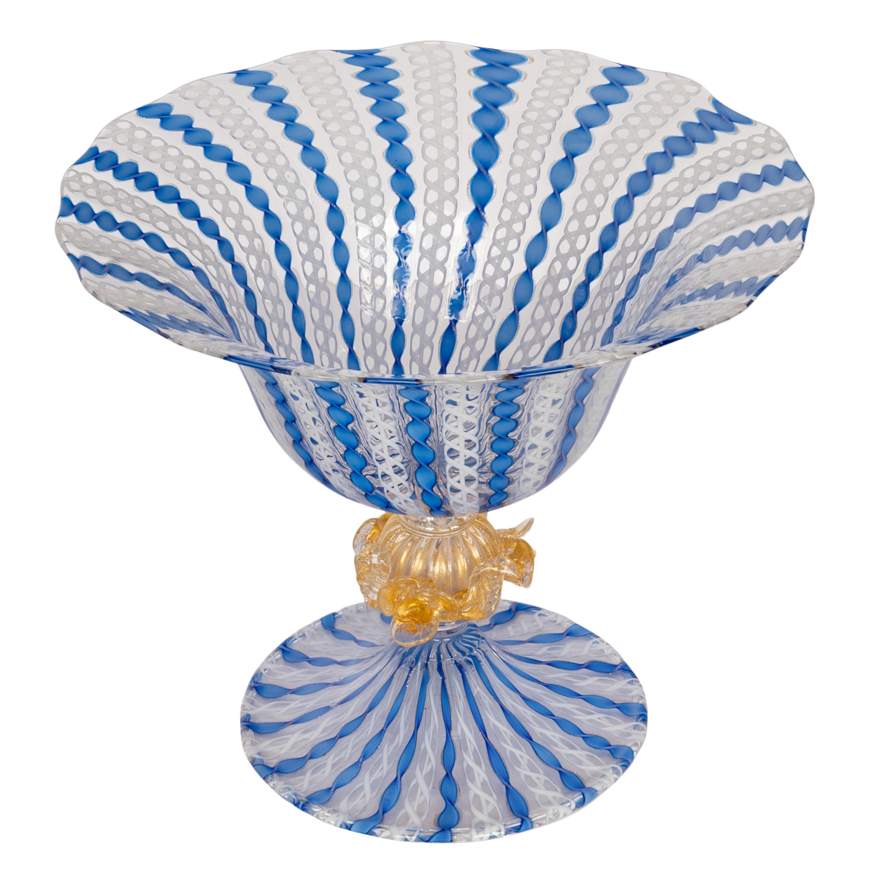 Un'antica ed elegante coppa o composta in vetro soffiato a mano di Murano Latticino, Italia, circa 1920. 
La grande ciotola svasata è formata da canne di vetro Latticino Zanfirico blu e avorio, al centro c'è una palla di vetro a coste con macchie di