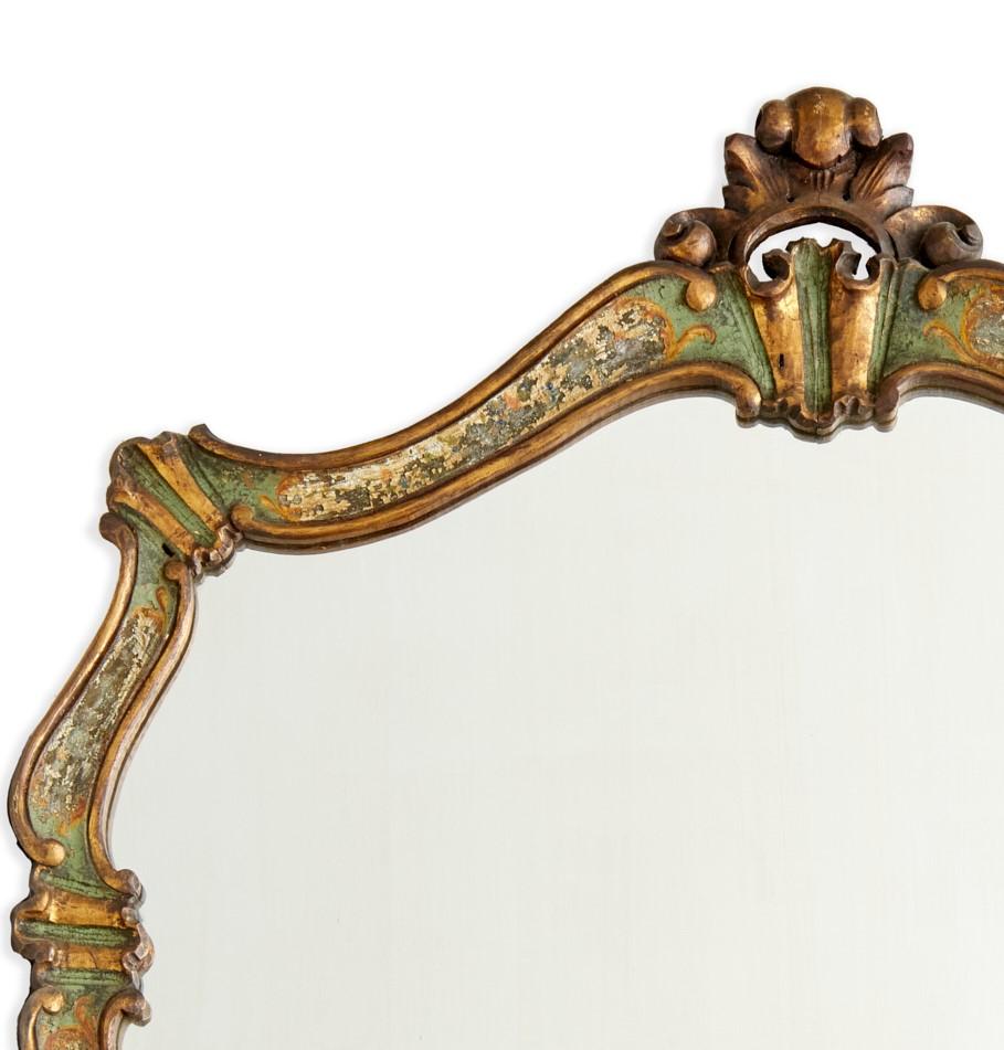 Late 19th/early 20th c., Italy, and antique Venetian Rococo polychrome painted and parcel gilt wall mirror. The shaped mirror glass is framed by an undulating gilt and polychrome painted scroll border with a top crest. The surface is attractively