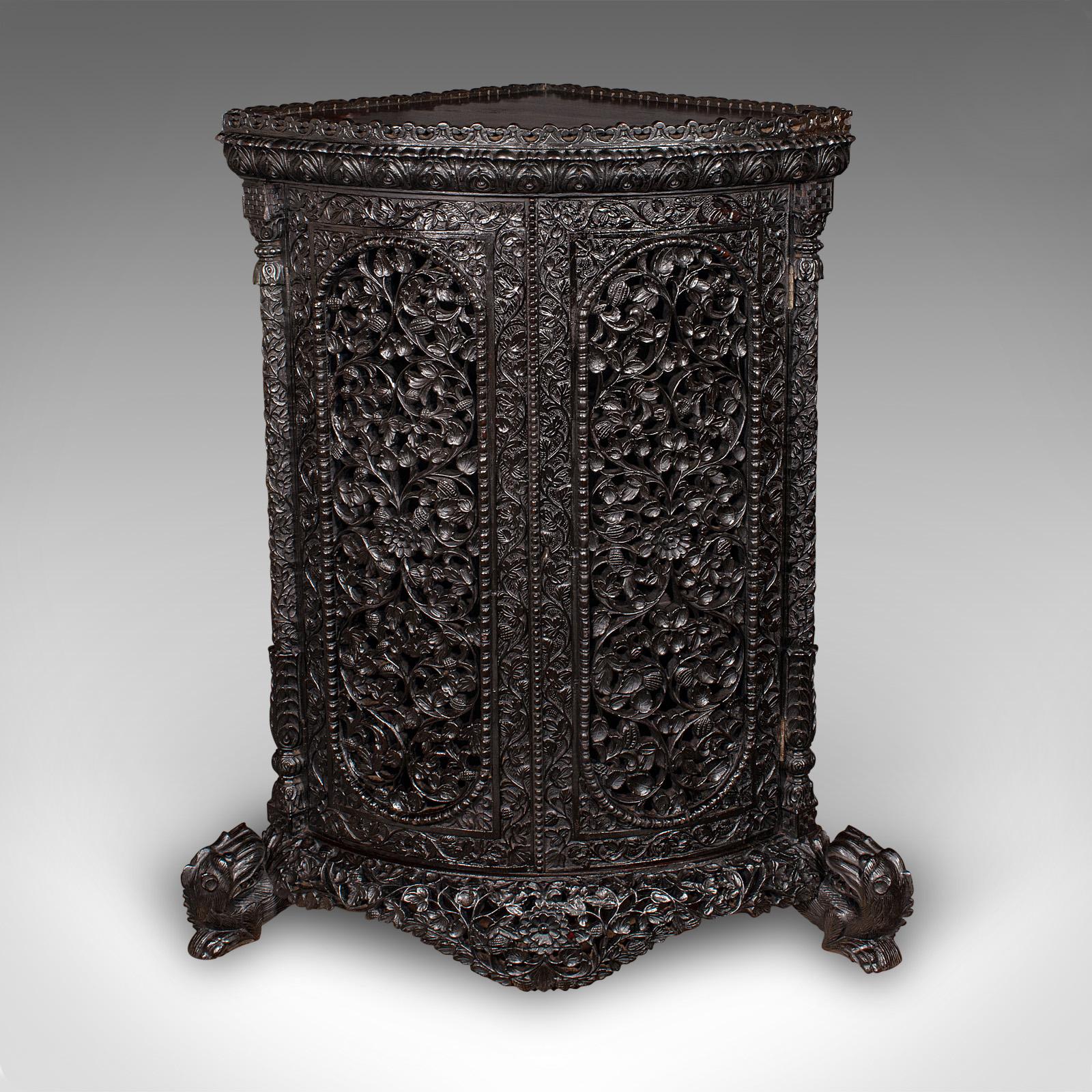This is an exceptional antique veranda gin cabinet. A Ceylonese, carved teak corner cupboard, dating to the late Victorian period, circa 1880. Exquisitely detailed and rich in craftsmanship, this profusely carved piece exudes colonial elegance and