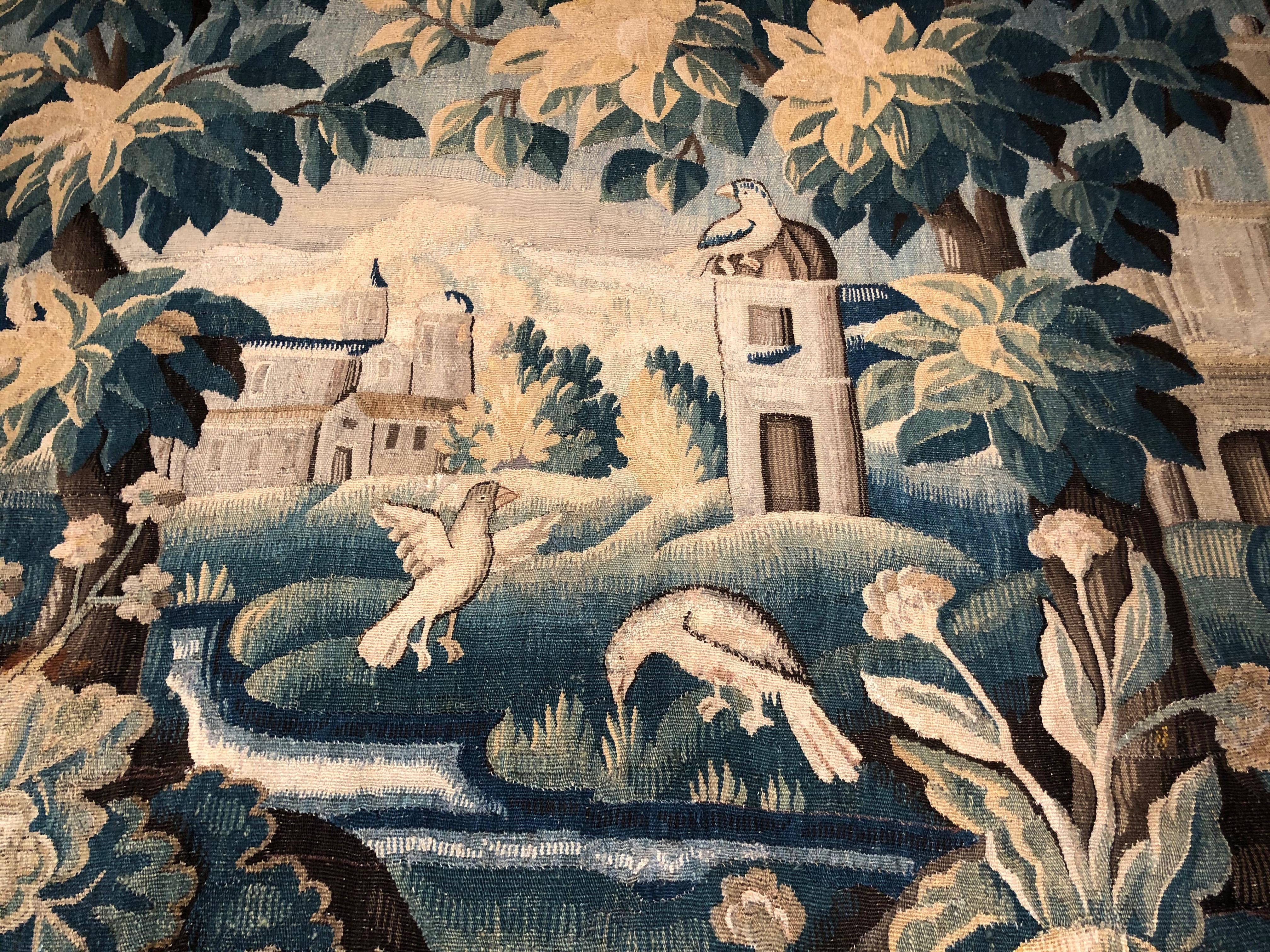 French, 18th century Verdure Aubusson tapestry handwoven in wool with silk highlights framed with a complete floral border. Two birds wade aside a winding stream in this scenic landscape with an ancient town in the rear, while the main focus of this