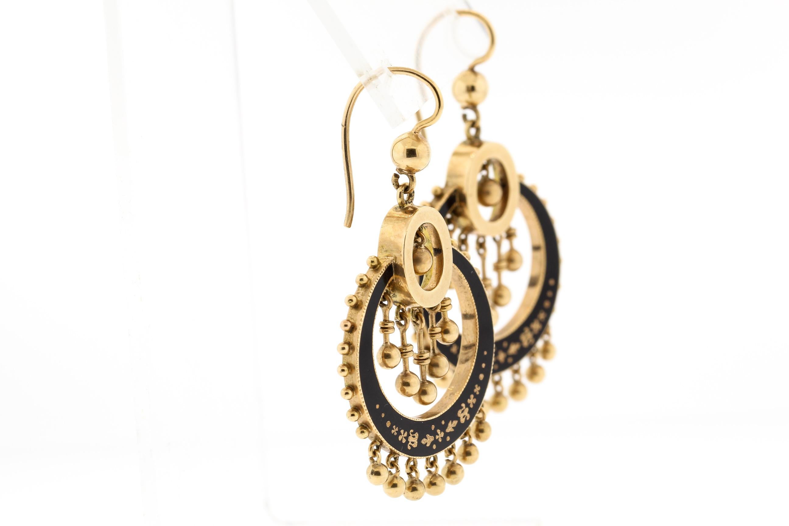 A feminine pair of antique Victorian black enamel earrings, circa 1880. This pair made in 14k yellow gold has beautiful gold balls hanging from the bottom, with the enter featuring a cascade of moveable gold bars with balls at the end. The earring