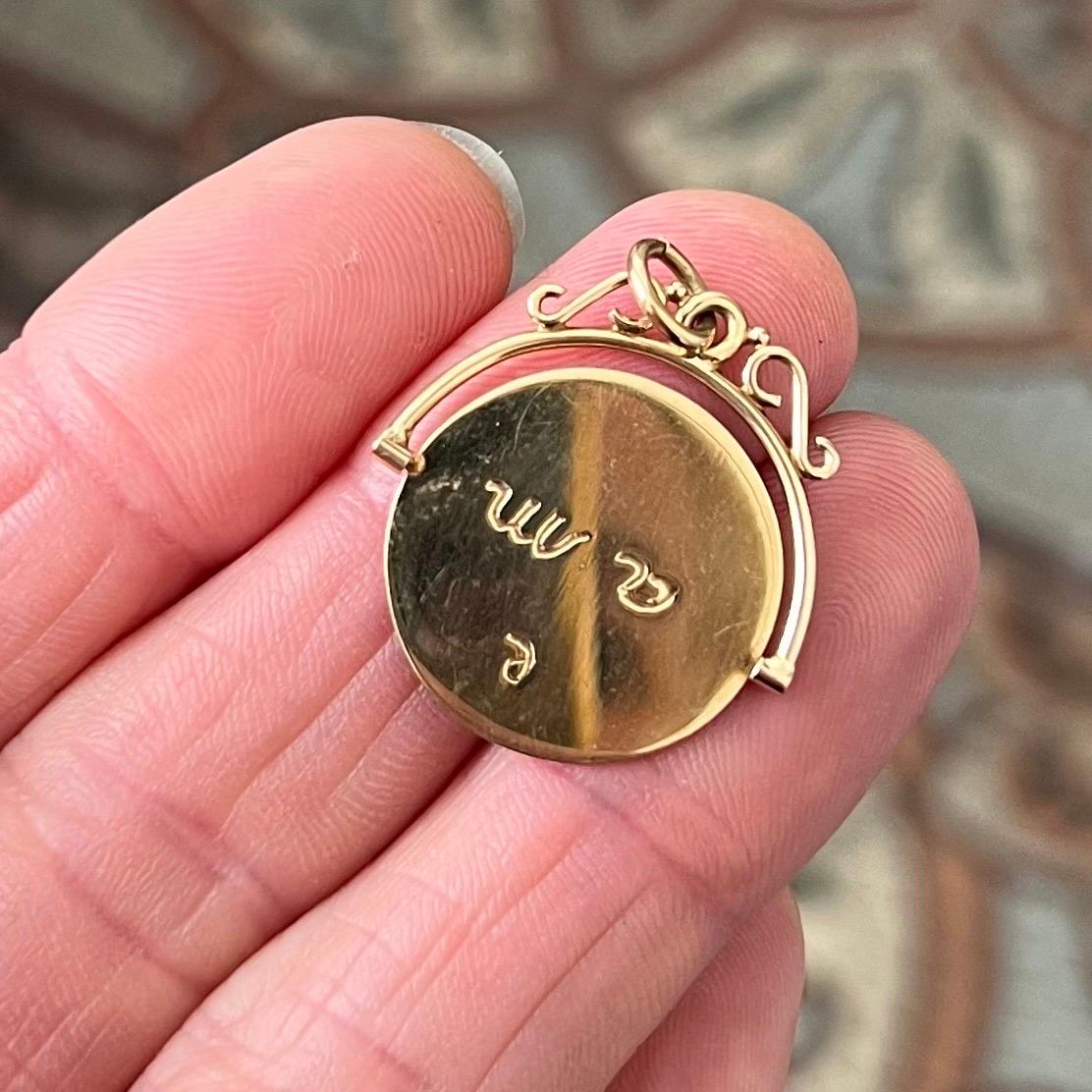Una romantica reliquia della fine del XIX secolo, questo antico ciondolo a forma di trottola è realizzato in oro 14 carati e presenta un disco rotante inciso a mano con la frase francese 
