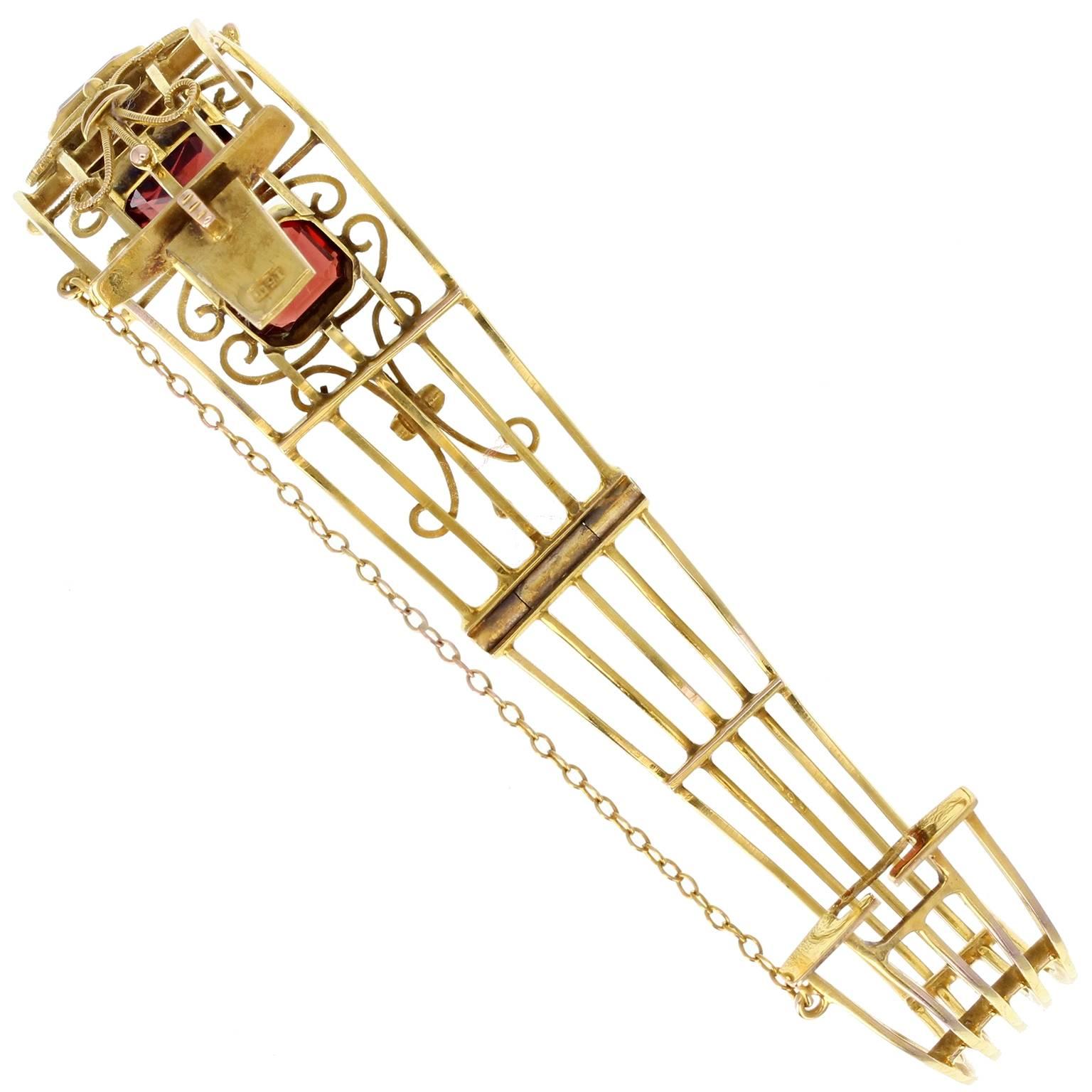 A fine quality Victorian openwork 15 carat gold bangle, set with three emerald-cut garnets. Applied wire scroll detailing. Hinged, with tongue-type clasp and safety chain. Stamped 15ct. 
Setting
Tests as 15ct gold

Diameter (wrist size)
60mm
