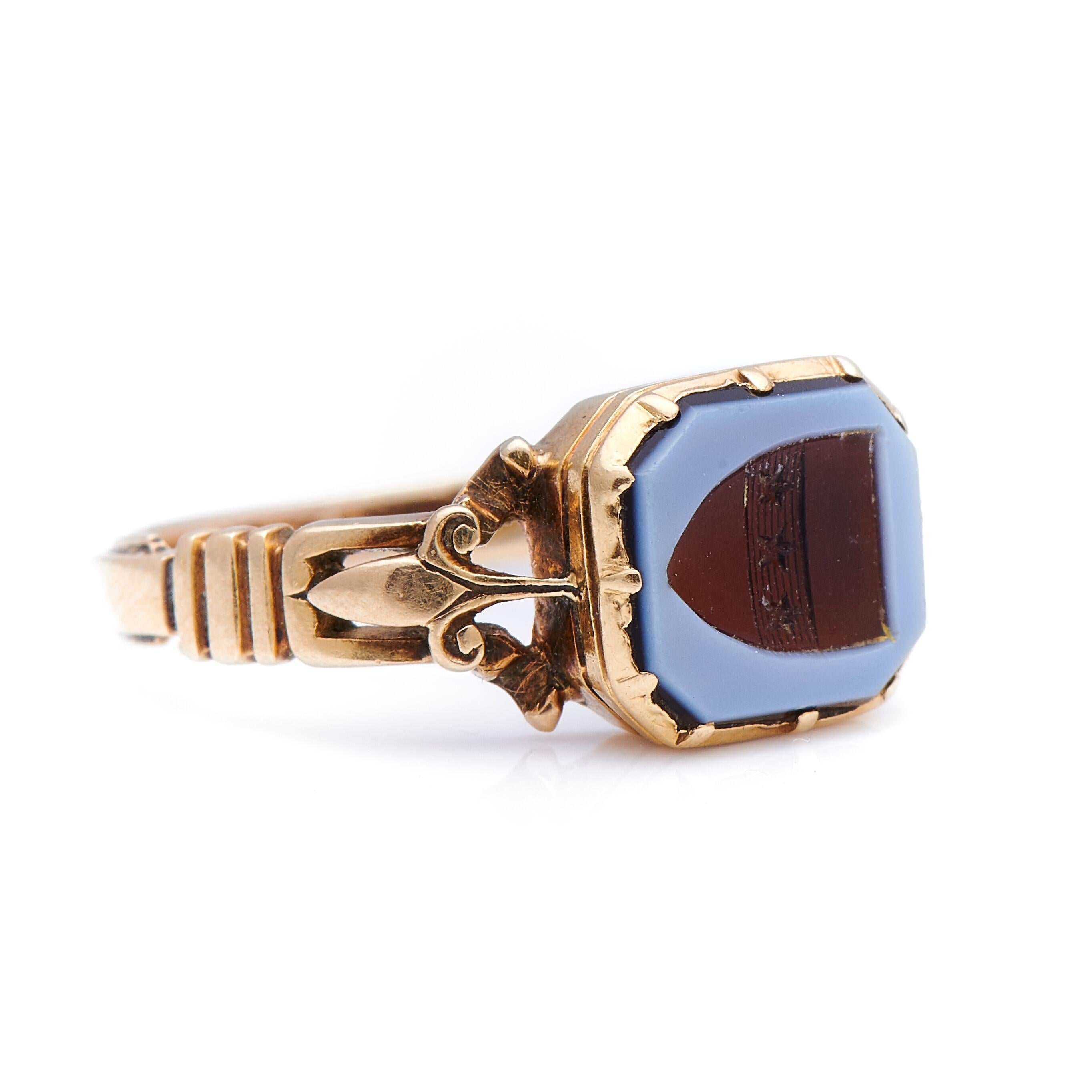 Carved agate signet ring, circa 1880. A striking ring, a beautiful carved agate, depicting a family crest, sits to centre in a simple but visually stimulating ribbed rub-over setting with skilful Fleur-de-lis style gold work shoulders; a true