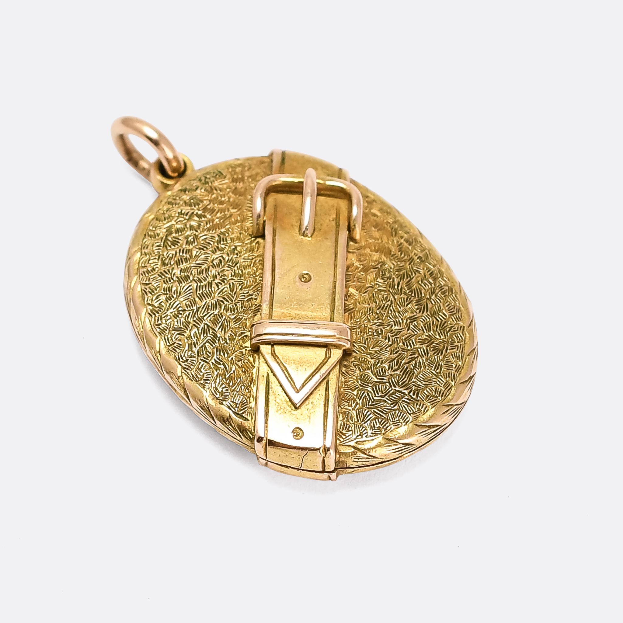 A cool, smaller scale, antique locket with belt and buckle motif wrapped diagonally around the oval body. The background is beautifully textured, and it opens to reveal two oval compartments. Crafted in 15 karat gold and dating from the