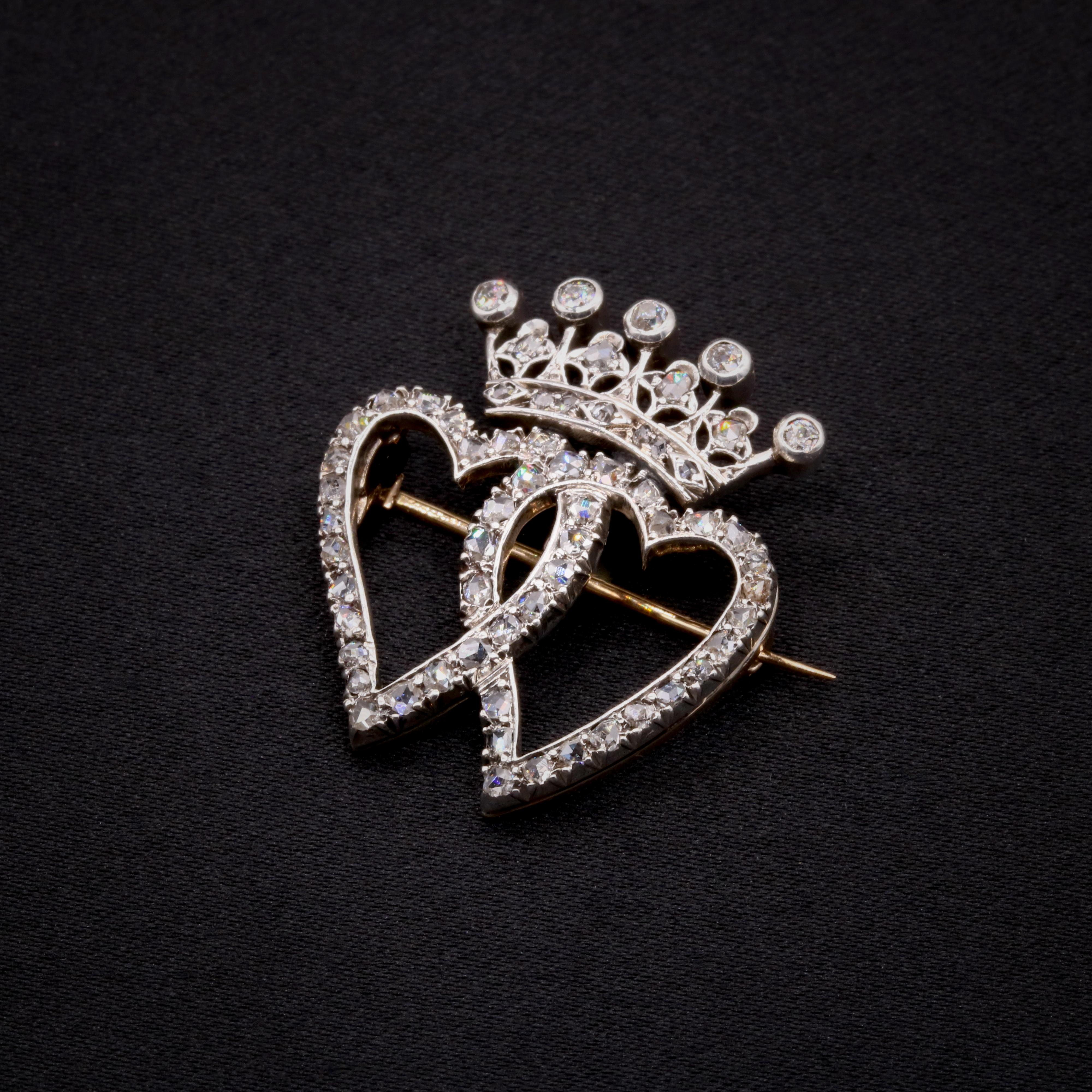 An antique diamond, silver, and yellow gold brooch, comprising five old European cut diamonds, and fifty-eight rose cut diamonds, in silver and 15 karat yellow gold. 

This Victorian brooch is designed as a pair of hearts, topped with a crown. The
