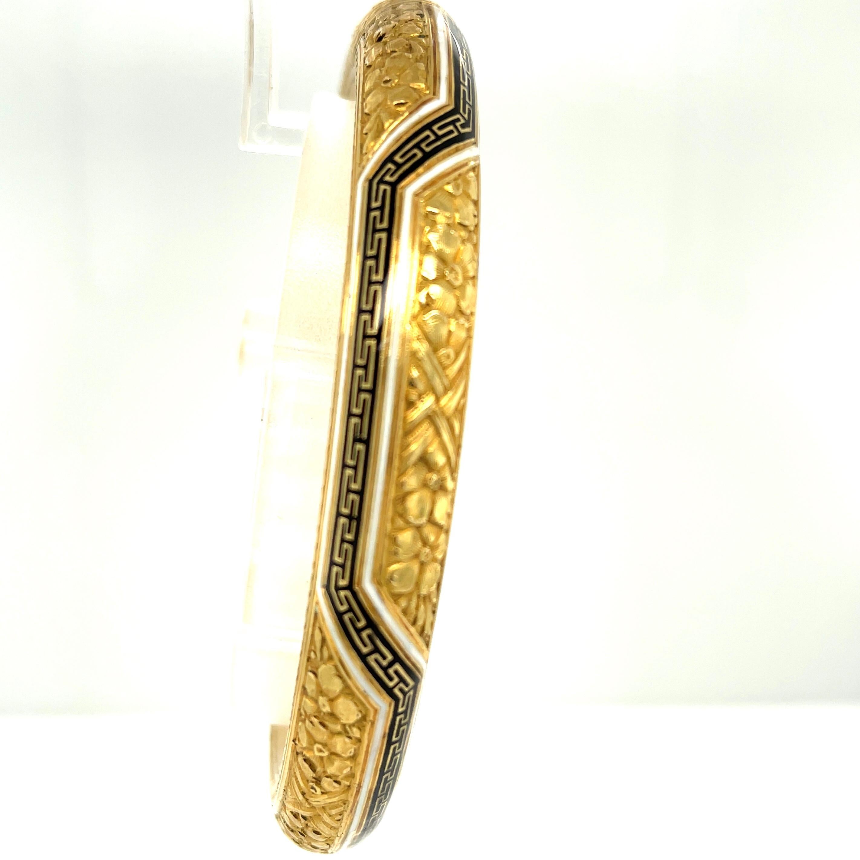 A rare 18k yellow gold hollow form bangle bracelet with beautiful engraving and  white and black enamel accents, circa 1880. This oval shaped bangle has a nice tubular width, with incredible craftsmanship. The engraving depicts five petal flowers