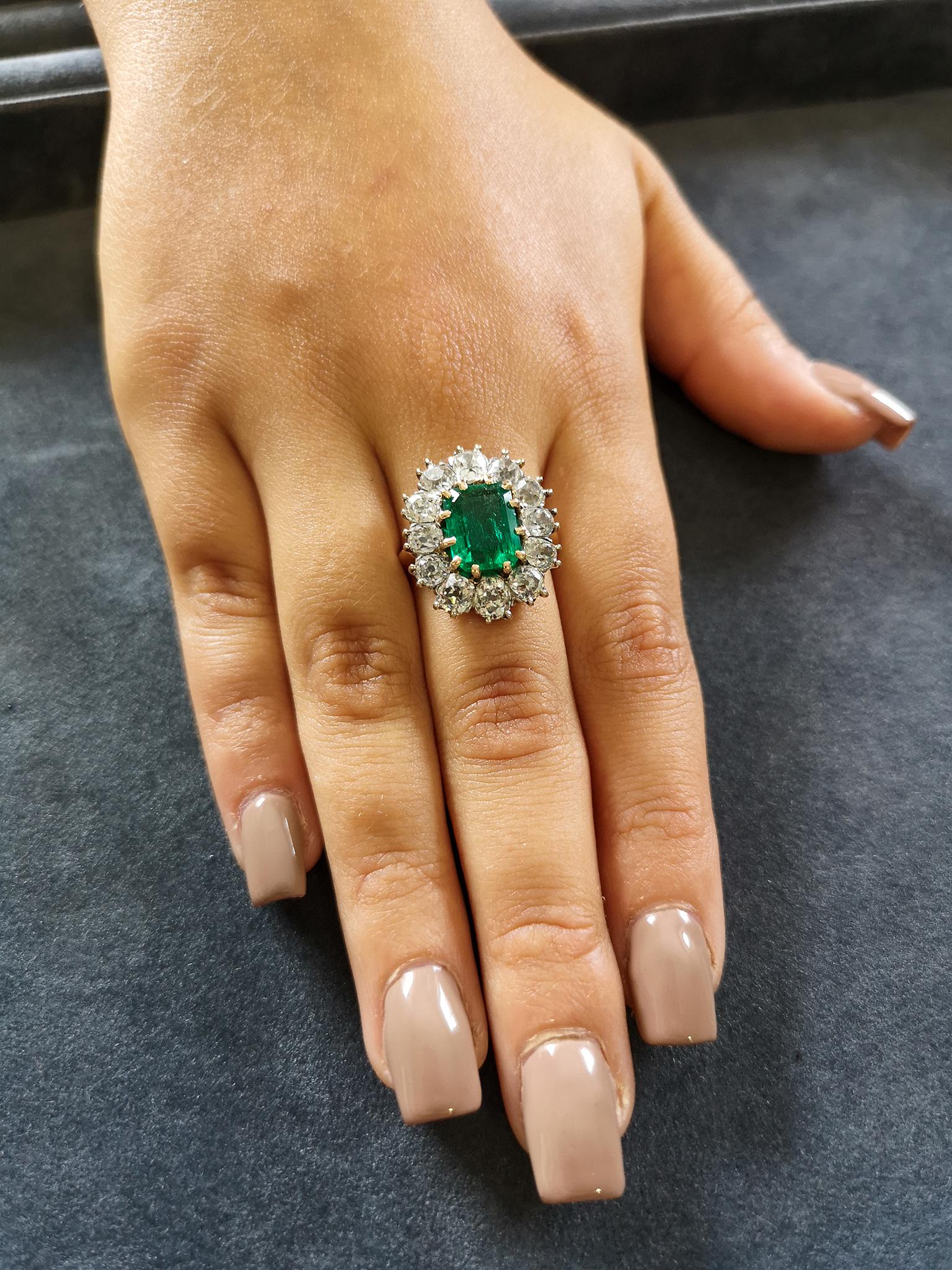 An exquisite, luscious deep-green emerald cut Colombian emerald of approximately 2.50 carats mounted in traditional 18-carat yellow gold claws, surrounded by 12 chunky, sparkling old mine-cut diamonds, totaling approximately 3.60 carats, H colour SI