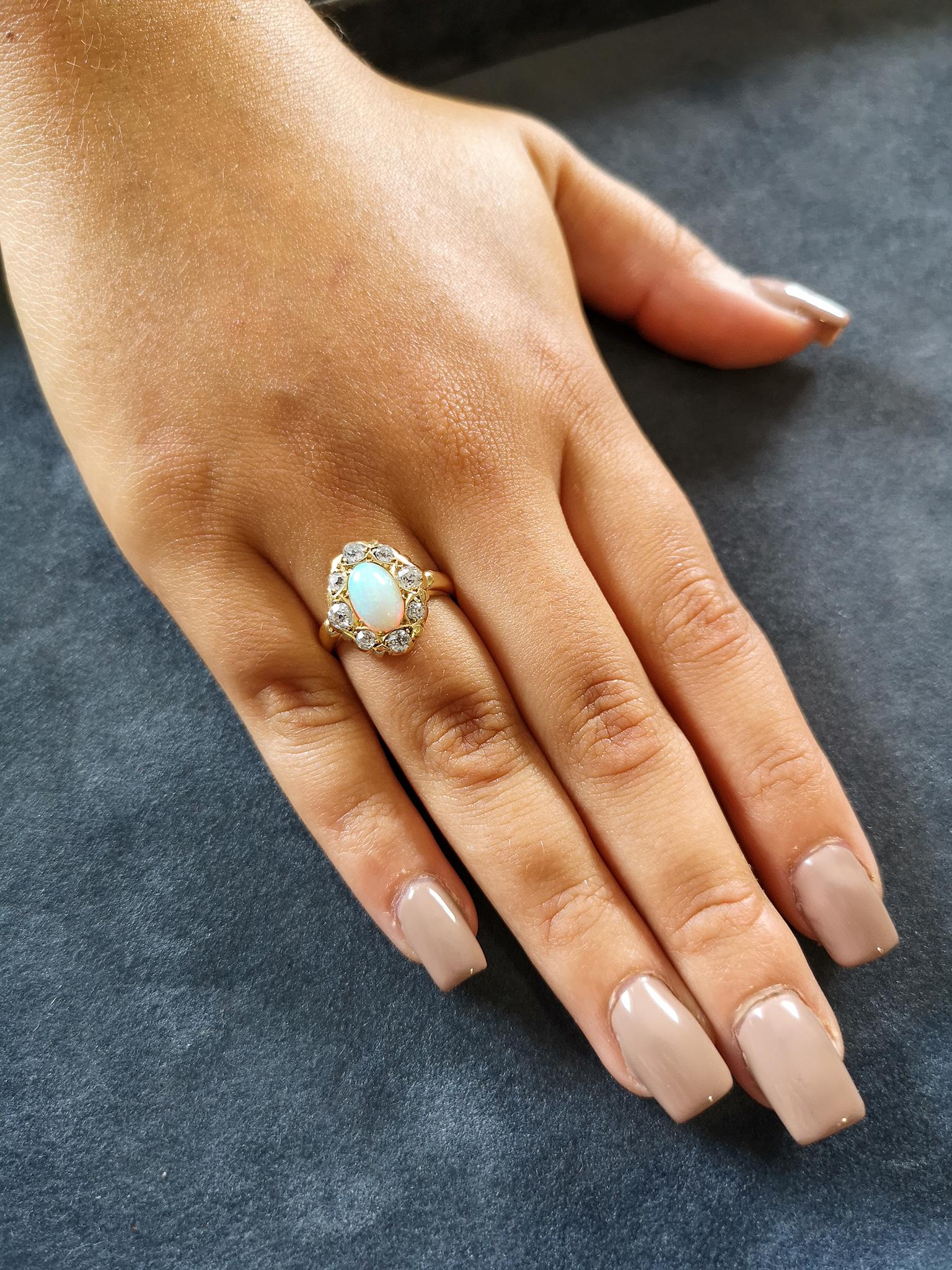 The fine quality oval cabochon opal, exhibiting excellent play of colour, predominantly greens and blues, surrounded by eight old-cut diamonds to form a fluted, lozenge shaped cluster. Approximately 0.50 of a carat in total, H colour, SI clarity. A