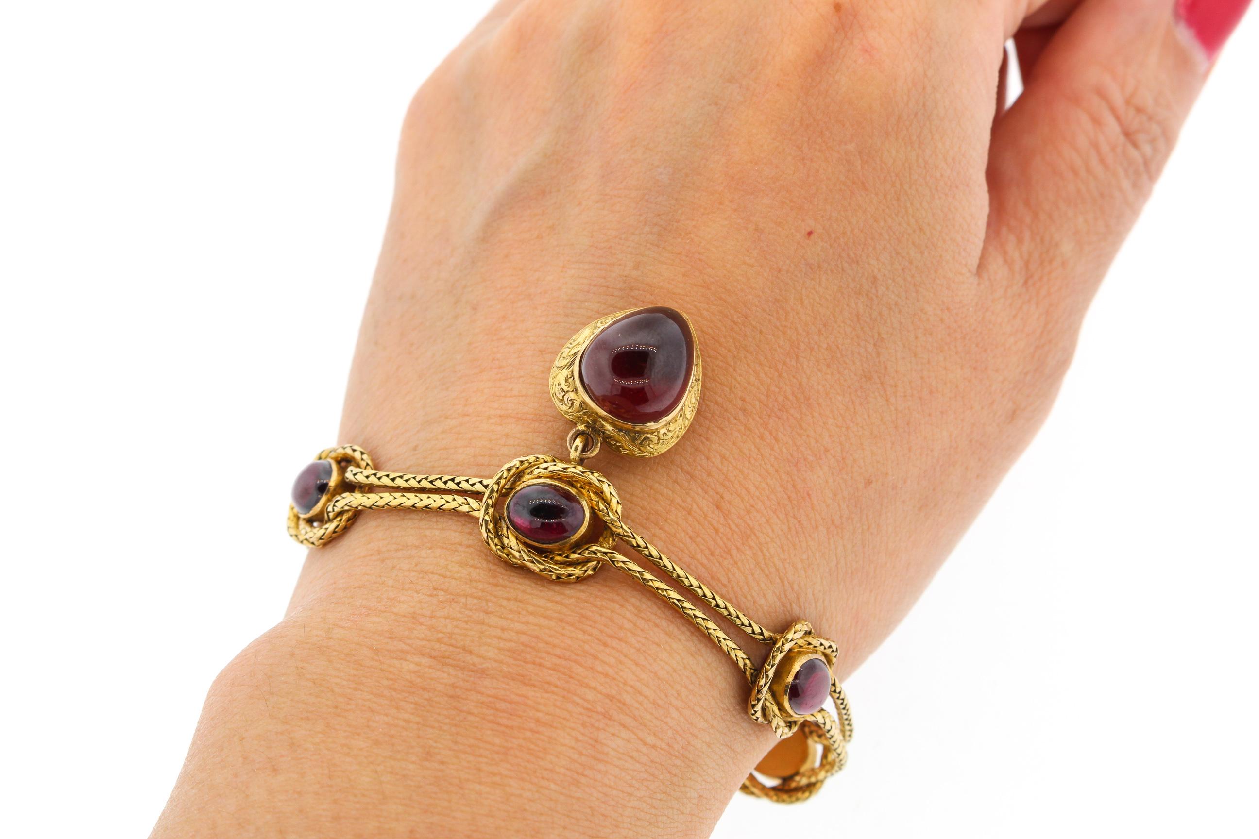 Antique mid-Victorian braided gold bracelet set with red carbuncle garnets and suspending a heart shaped locket, circa 1860. The gold bracelet knots around the oval shaped garnets in a delightful pattern. The large cabochon garnet in the heart is a
