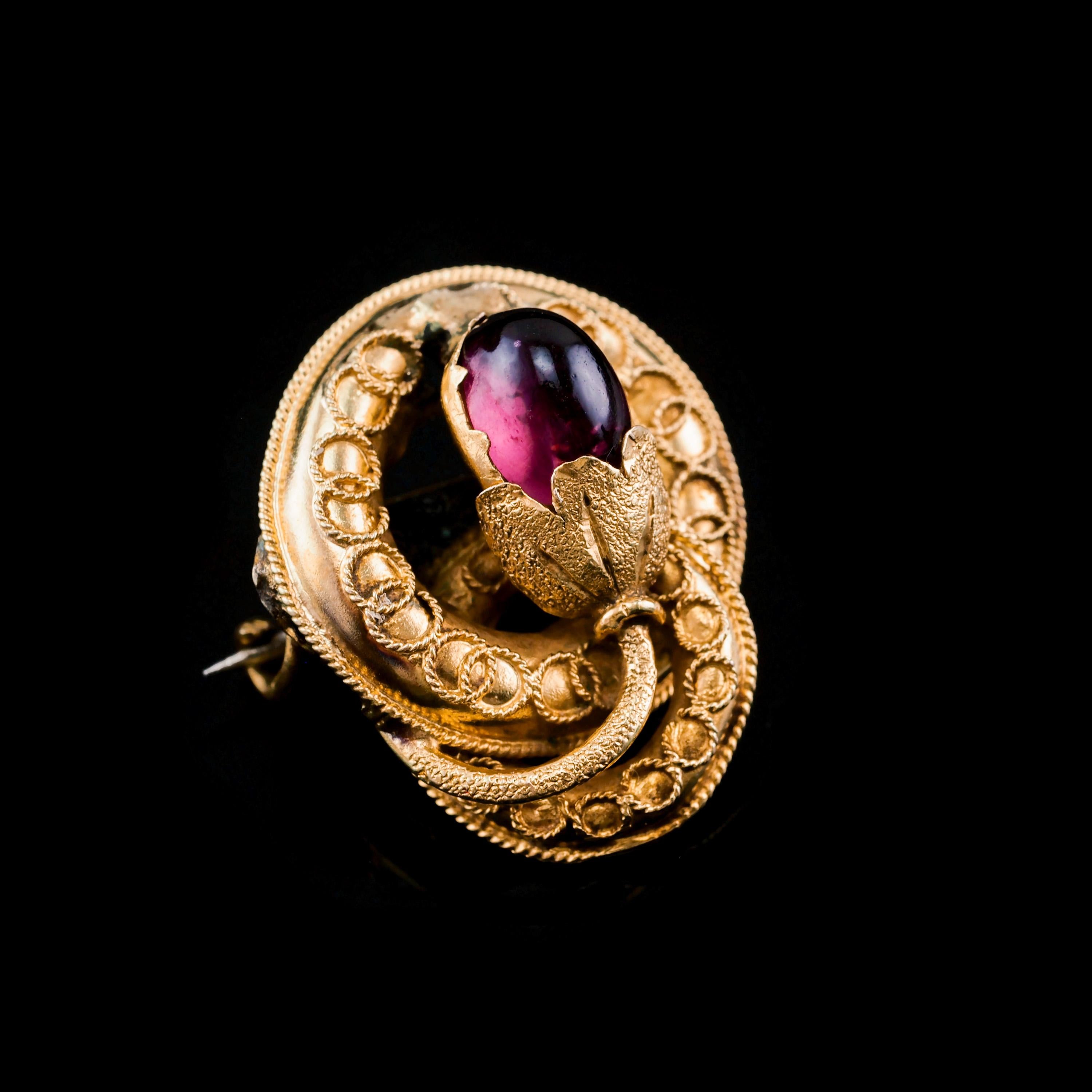 We are delighted to offer this sweet 18ct gold Victorian brooch made c.1880.
  
This brooch features a lovely intertwined circular design with the central flower bud being mounted with a garnet cabochon. 
 
The gold workmanship on this brooch is