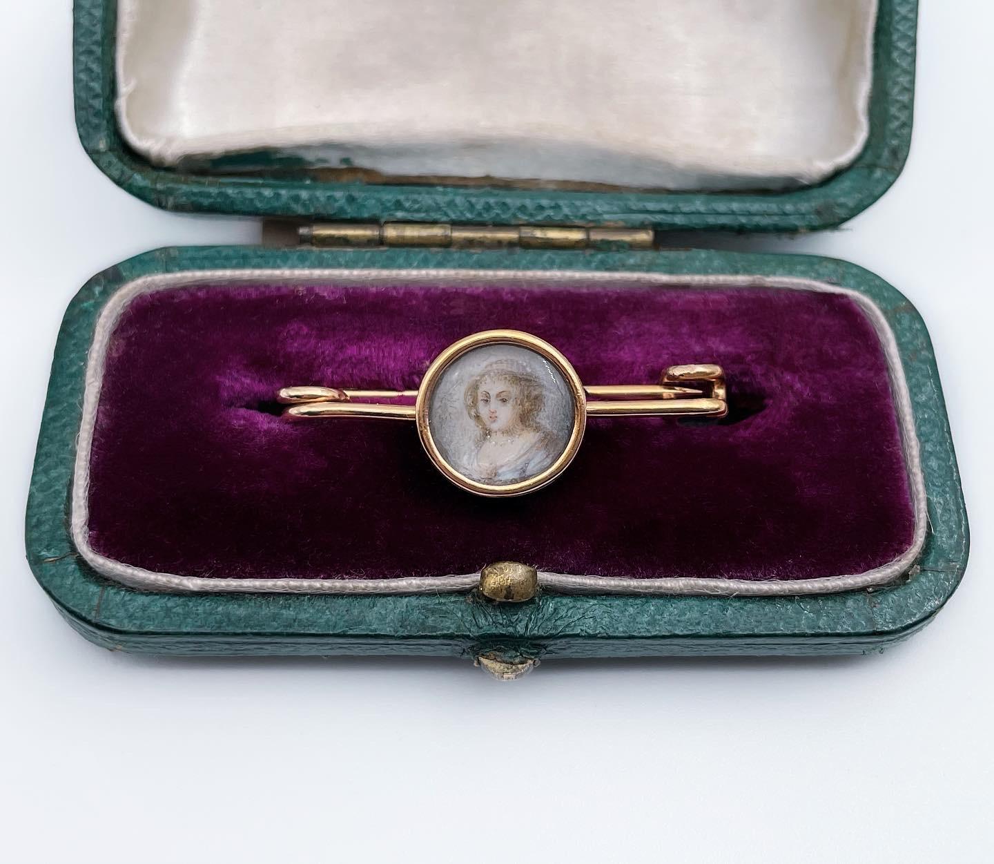 This is a delicate bar brooch dating from 19th century Victorian period. The piece is crafted in 18K yellow gold. It features a hand painted miniature portrait, depicting a lady. The picture is small and highly detailed.

The brooch has a safe