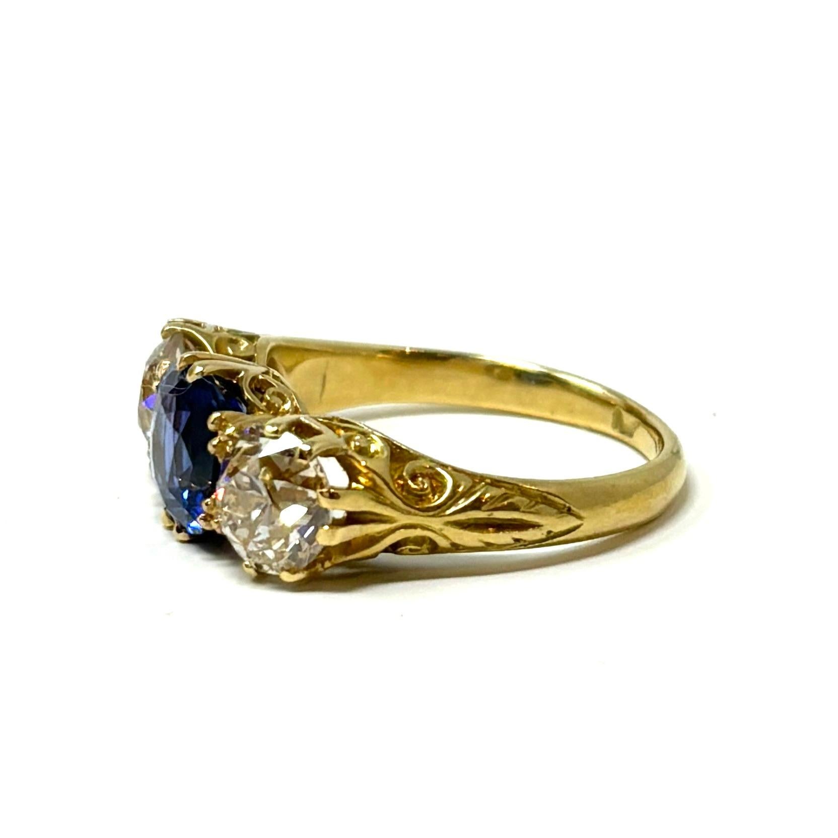 This antique three stone ring features a stunning vivid blue cushion cut sapphire weighing approximately 2.10 carats flanked by two old European cut diamonds which weigh approximately 2.10 carats total weight. The 18K scrolled gold mounting