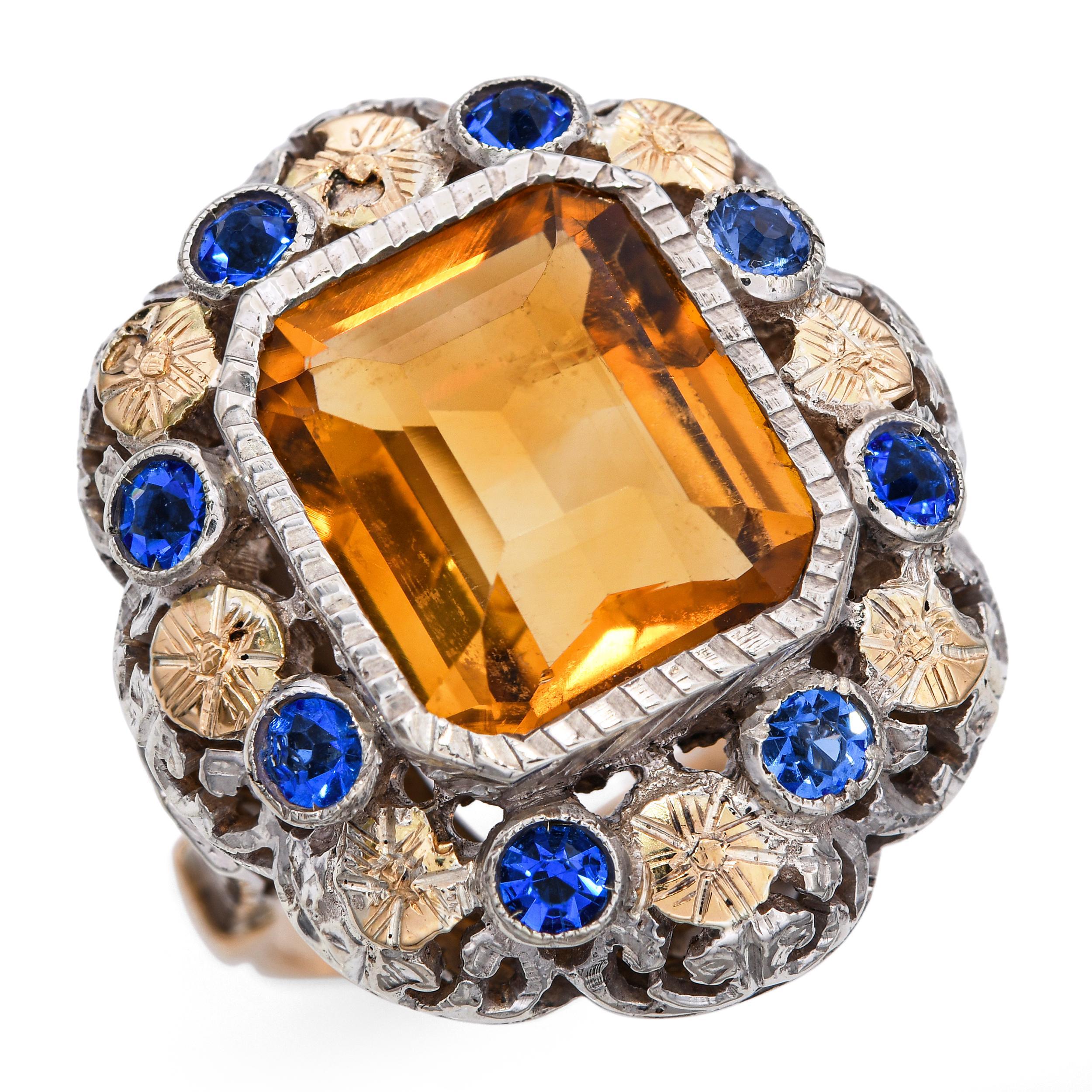 This antique Victorian cocktail ring is crafted in 18k gold, featuring an intricate floral motif with yellow gold flowers delicately framed in silver. At its center rests a warm citrine gemstone surrounded by glimmering paste stones, capturing the