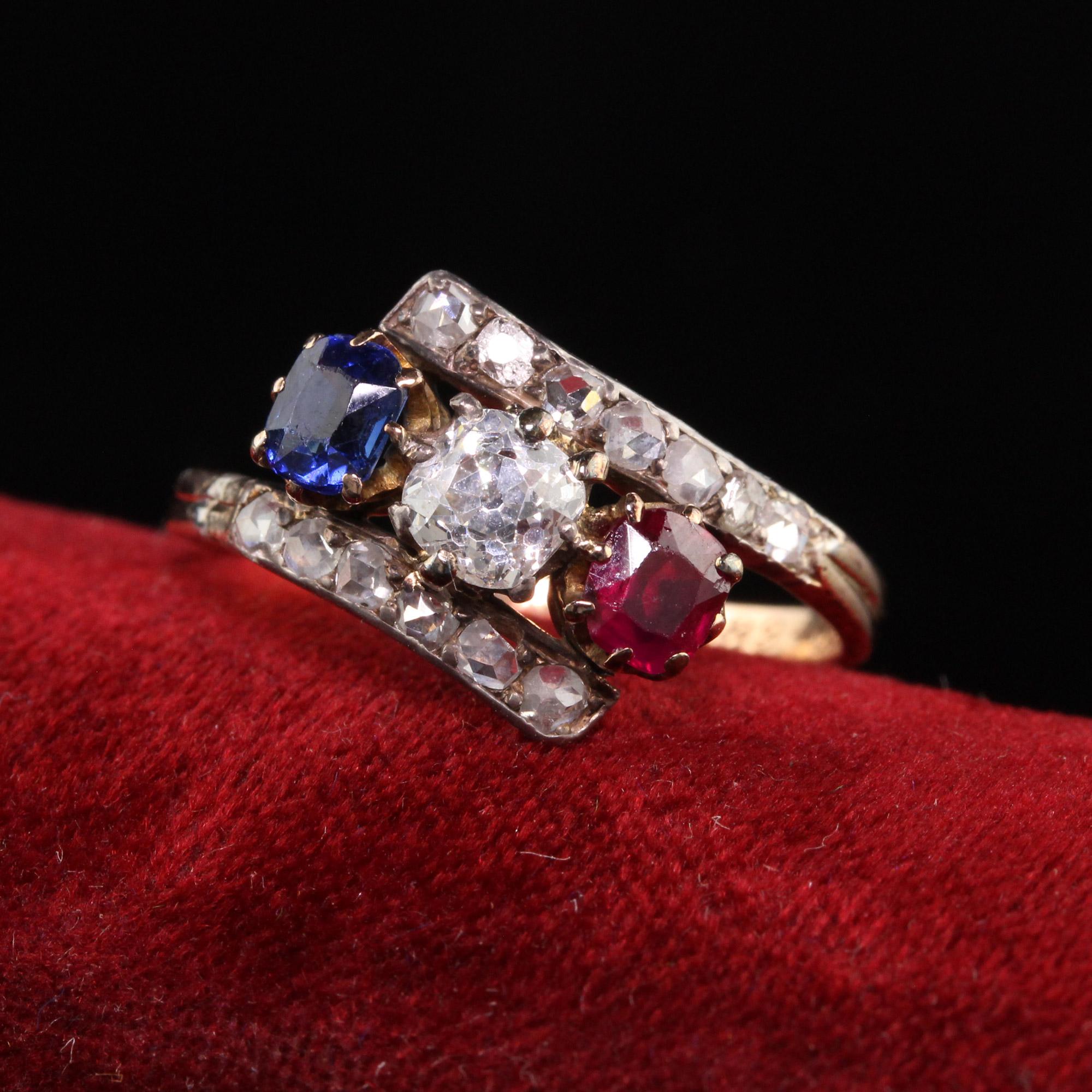 Beautiful Antique Victorian 18K Yellow Gold Diamond Ruby Sapphire Three Stone Ring. This incredible ring features an old mine cut diamond, natural ruby, and natural sapphire surrounded by chunky rose cut diamonds. They are set in a gorgeous