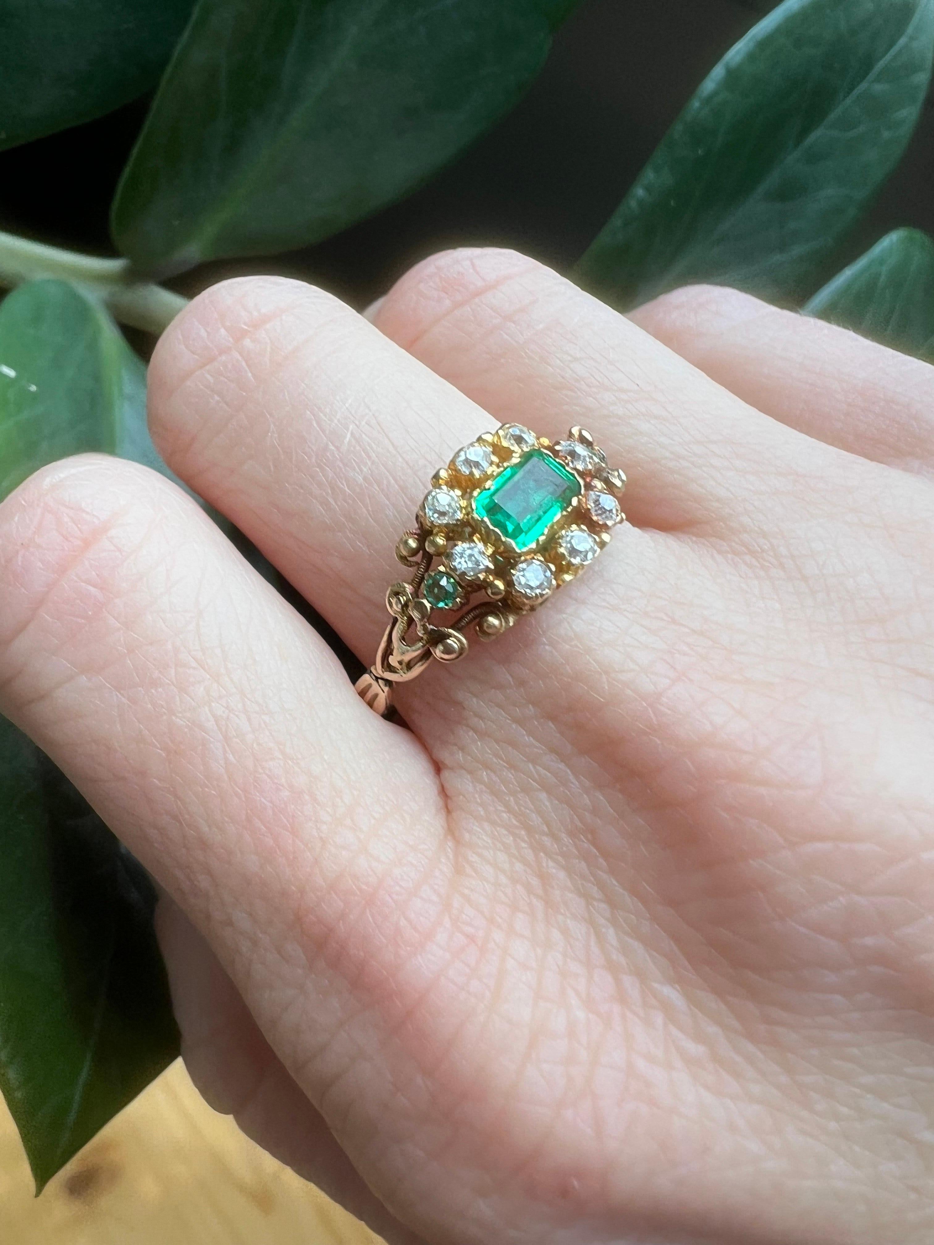 Antiker viktorianischer 18kt Gold Smaragd Cluster Ring.

Der Ring hat ein Cluster-Design und ist aus 18 Karat Gelbgold gefertigt. In seinem Zentrum befindet sich ein rechteckiger Smaragd im Stufenschliff, der in Zacken gefasst ist und einen