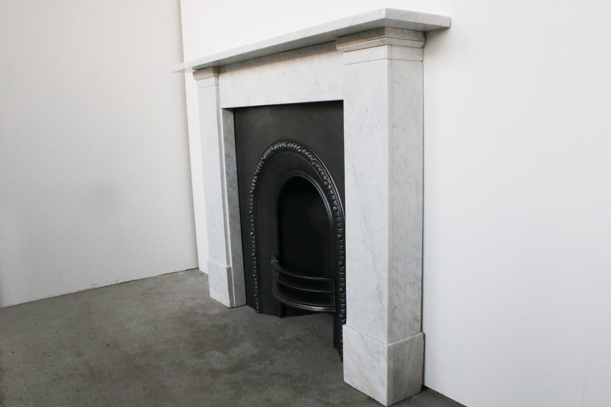 An antique late 19th century Victorian Carrara fireplace surround, of simple form with full height jambs terminating in a recessed band and simple interruptions below the shelf, circa 1850.

Pictured with an original cast iron and tiled grate sold