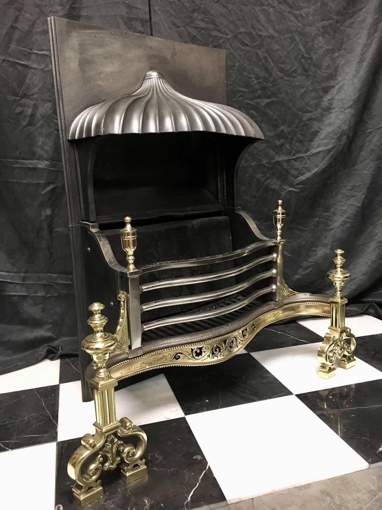 A large inset antique Victorian 19th century hooded neoclassical style cast iron and brass fire grate basket. The polished serpentine four barred grate surmounted by tall brass finials connected by scalloped basket sides supporting a high front with