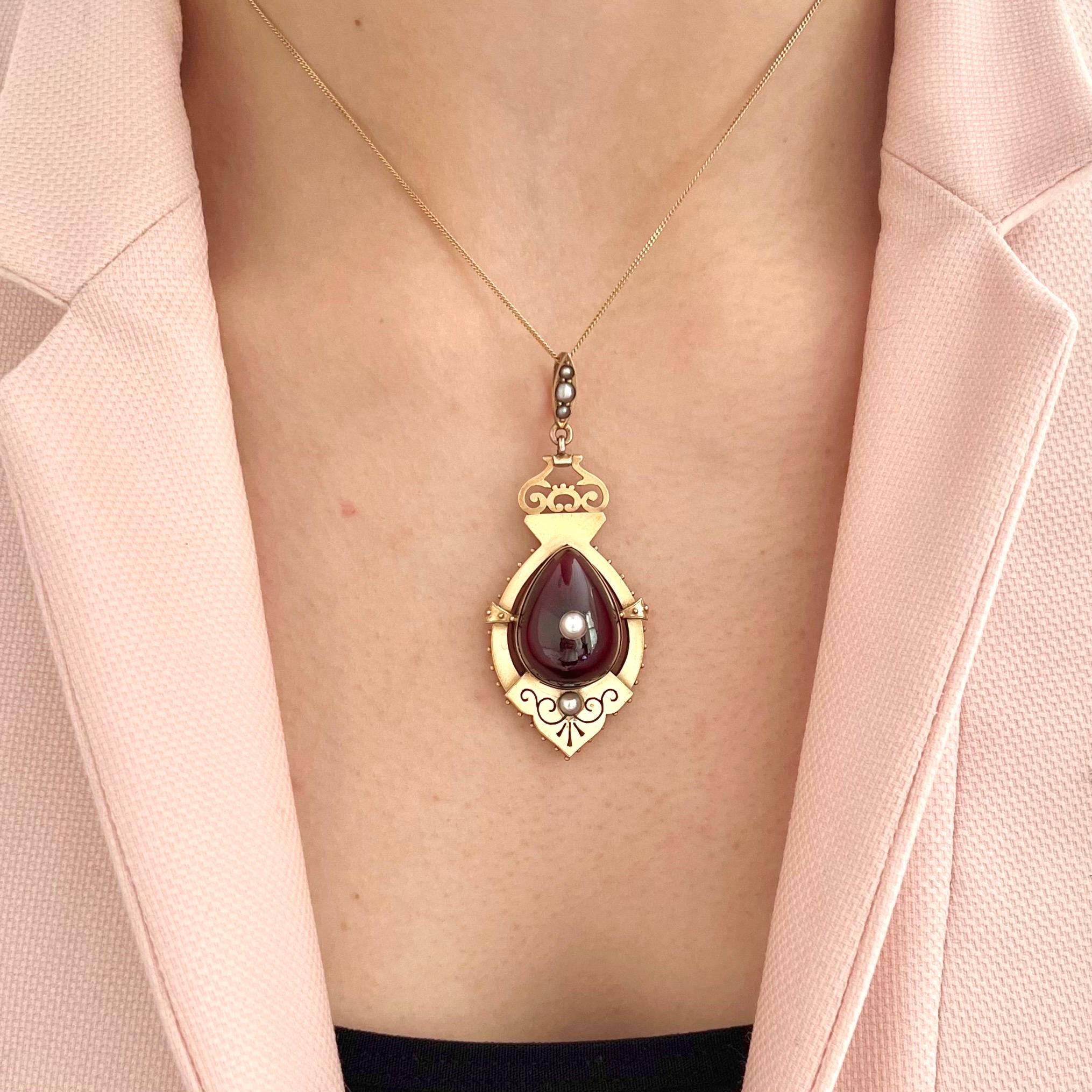 A beautiful example of Victorian jewelry, this ornate locket pendant is crafted in warm 9K yellow gold and showcases the elegant craftsmanship of the era. The focal point is a deep red, cabochon-cut garnet carbuncle, shaped in a teardrop form and