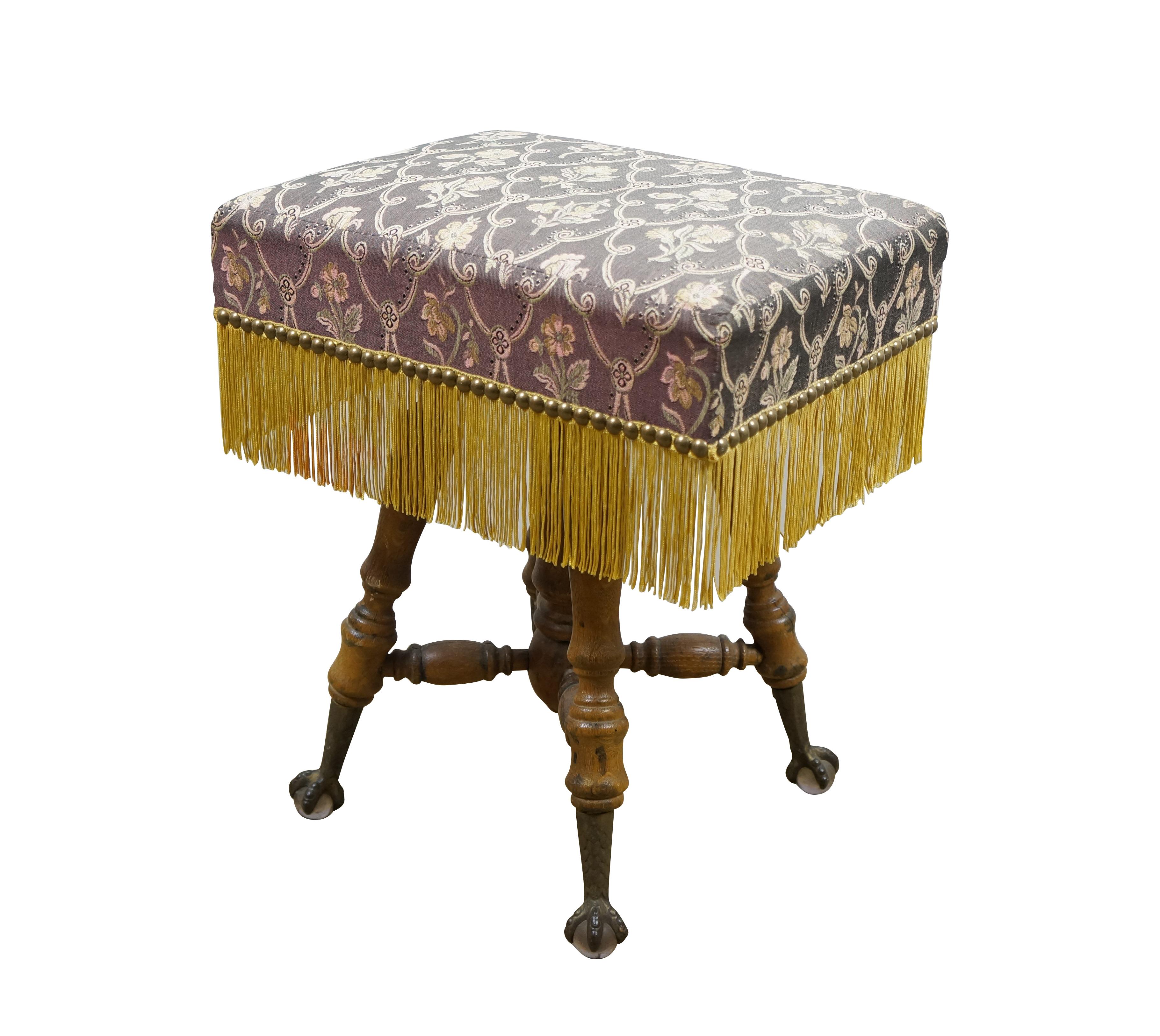 Circa late 19th century piano stool / foot rest / ottoman featuring four turned legs with glass ball and claw feet and rectangular seat upholsted in purple and gold floral brocade with golden fringe and nailhead trim. Le siège se dévisse du montant