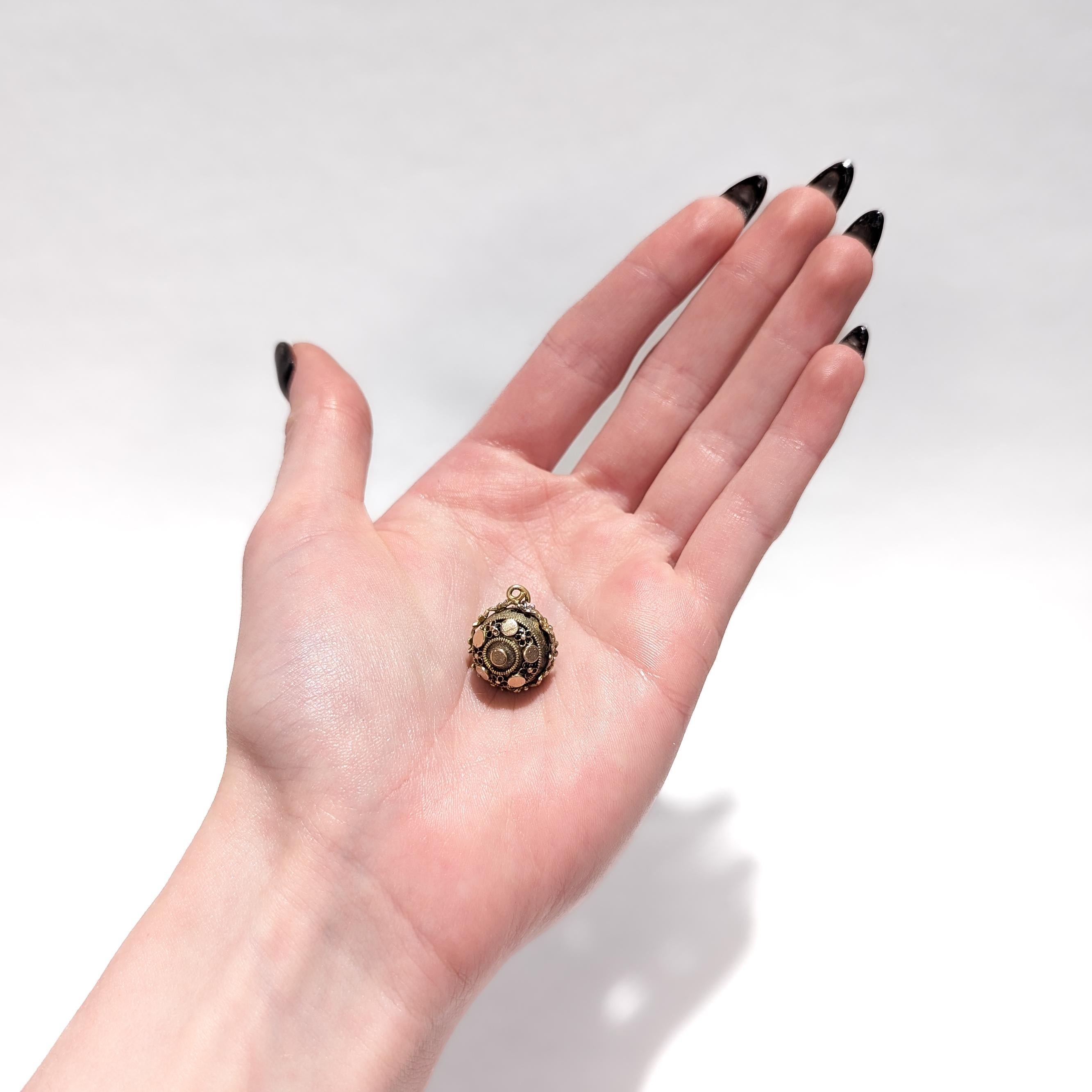 A fine antique gold-filled Aesthetic Movement charm.

With a gold-filled spherical body.

Having a ring of applied flower devices with white enameled petals around the circumference. The faces of the sphere with alternating applied circles & flowers