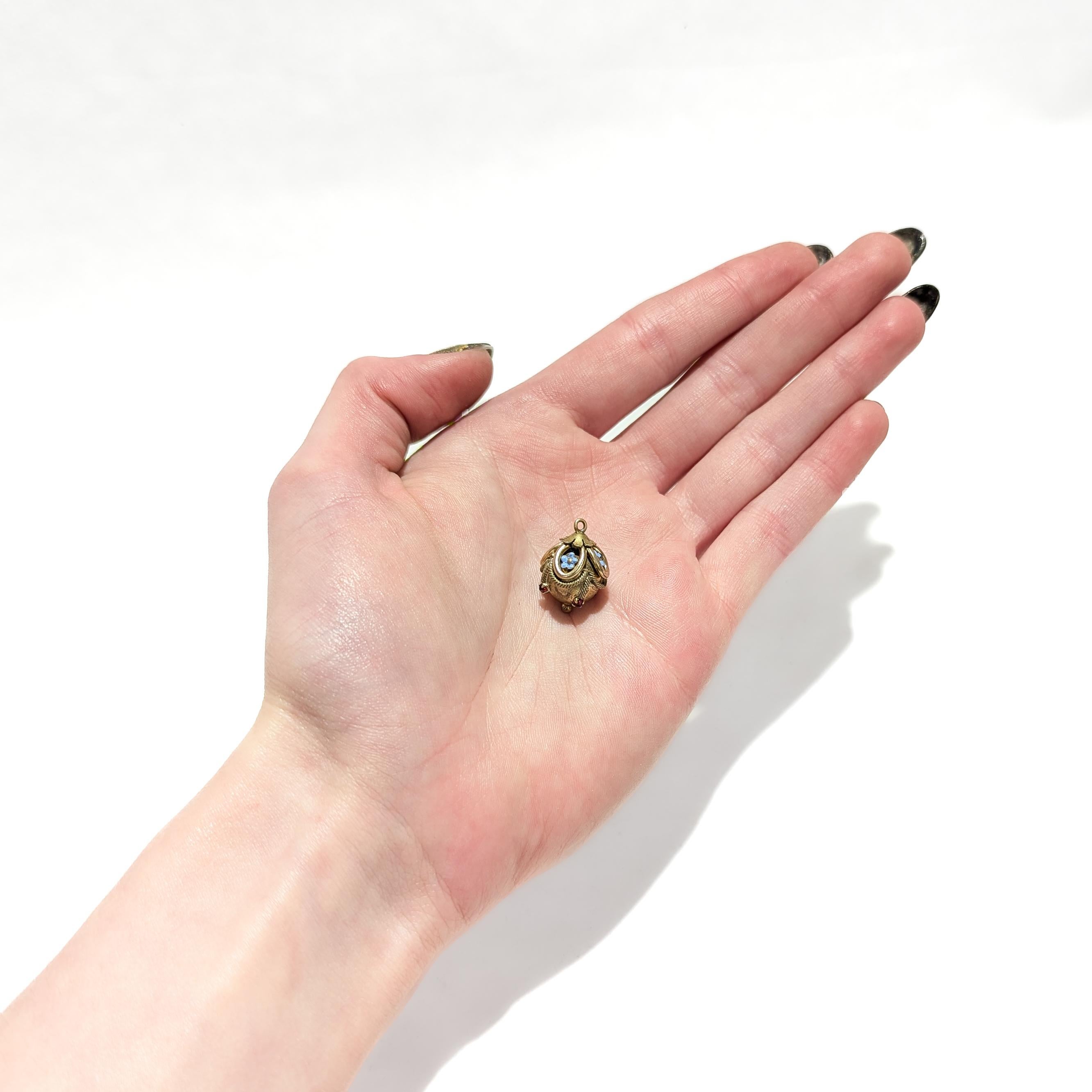 A fine antique gold-filled Aesthetic Movement charm.

With a gold-filled spherical body.

Having applied wirework and floral motifs throughout.

With 4 enameled flowers and 4 prong-set garnets.

The top set with an integral jump ring and bail; the