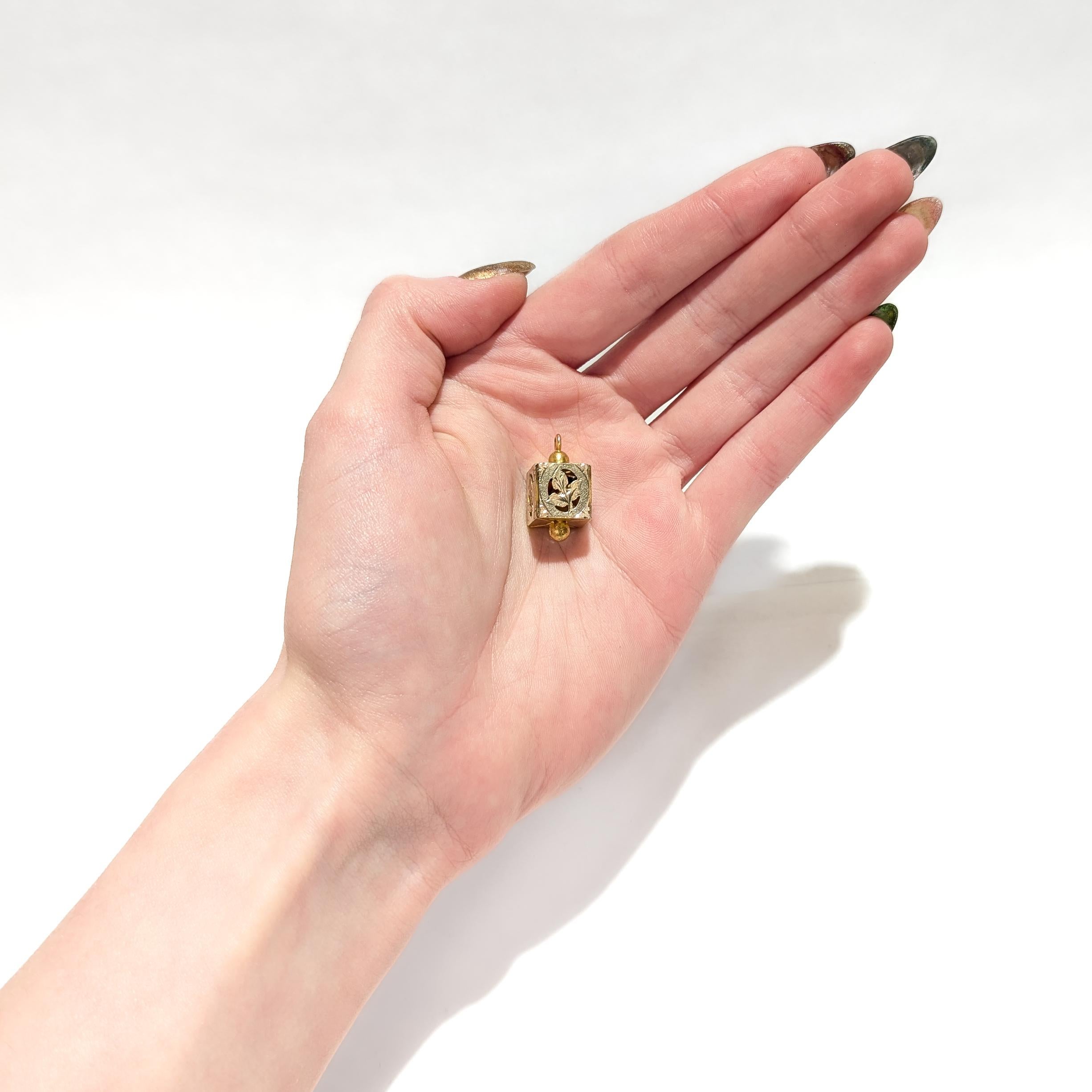 A fine antique gold-filled Aesthetic Movement charm.

With a gold-filled body.

In a cube shape with openwork leaf designs to the sides. 

The top with an integral bail. The bottom with a reverse ball finial.

Simply a wonderful Aesthetic Movement