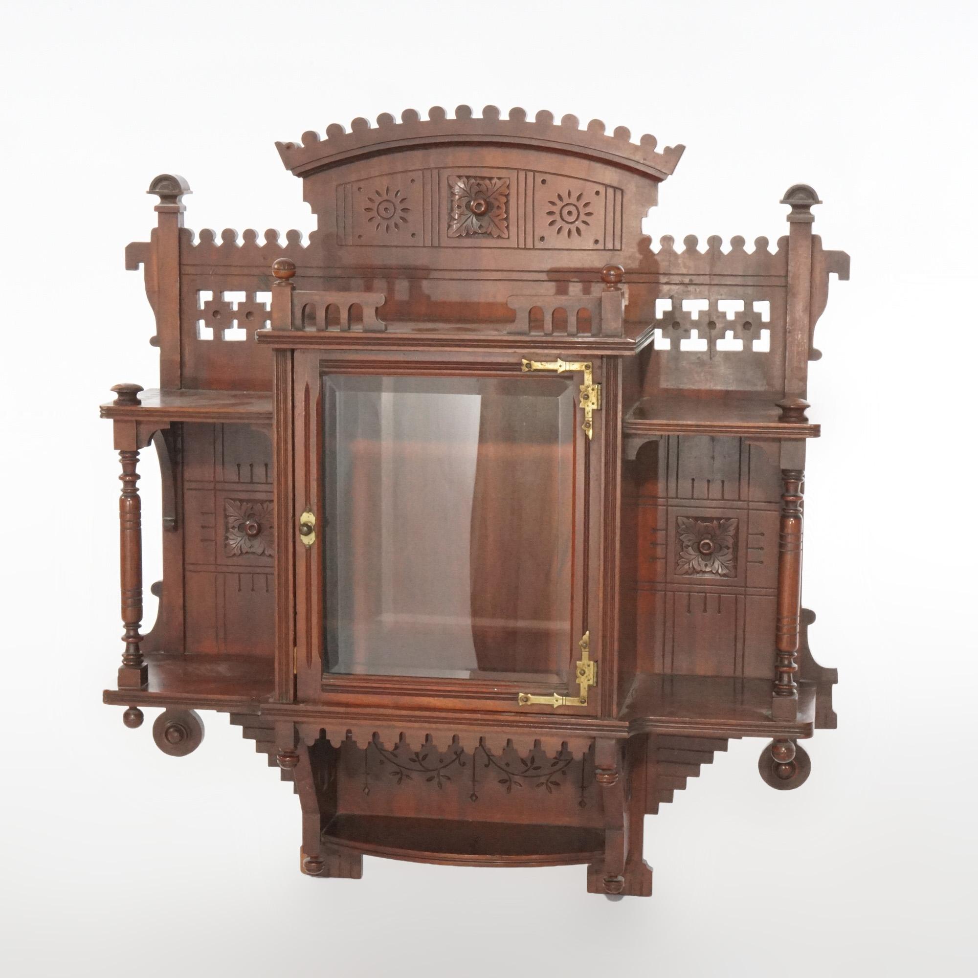 An antique Victorian Aesthetic mirrored wall cabinet offers mahogany construction with central compartment with glass door and having flanking display shelves, carved element throughout, circa 1890

Measures- 32'' H x 29'' W x 8 1/2 D.