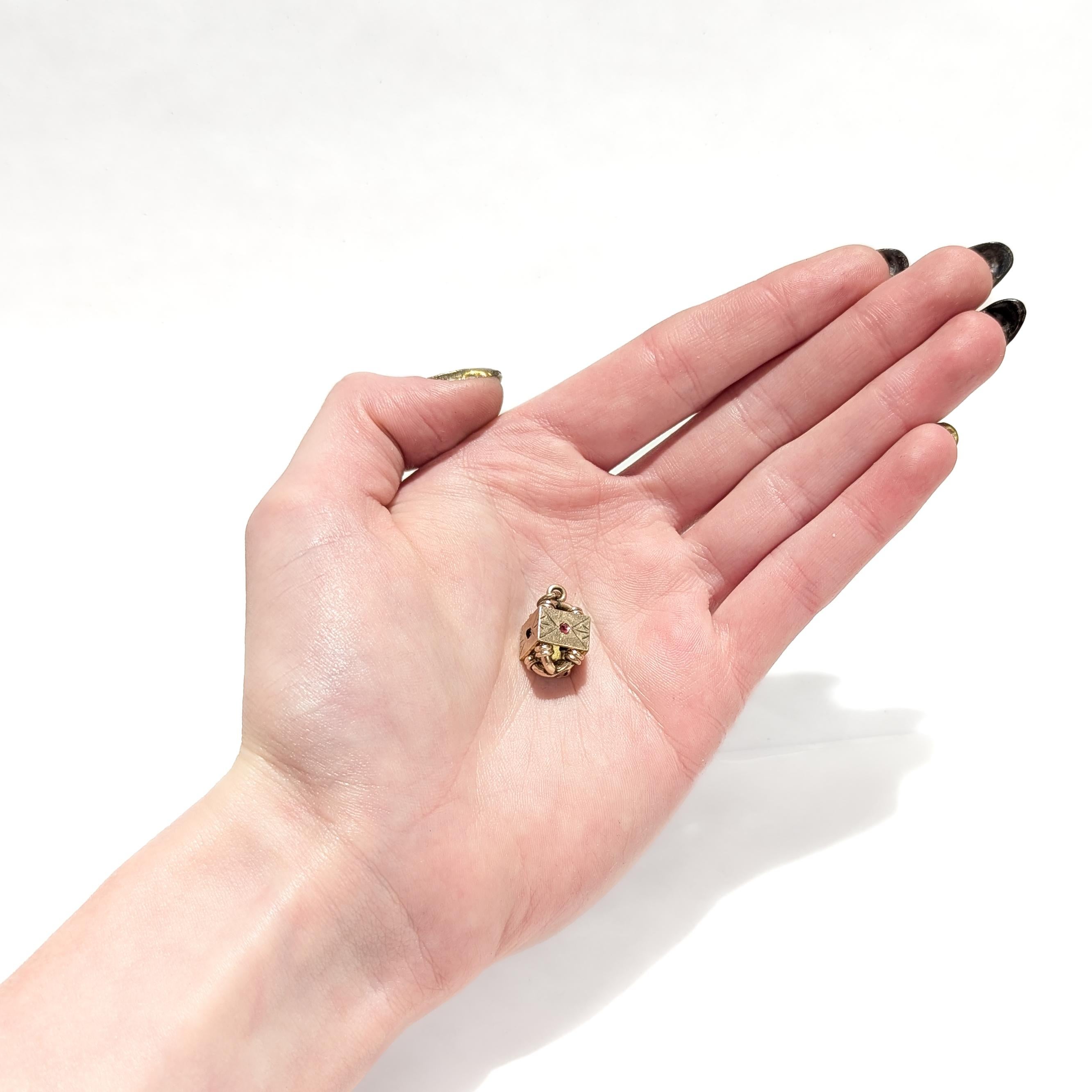 Pendentif ou charme en forme de porte-montre.

Avec un corps architectural rempli d'or.

Avec des cabochons en verre sertis sur la lunette et des gravures sur l'ensemble de la pièce.

Avec un anneau de sécurité ou un anneau de saut intégré et