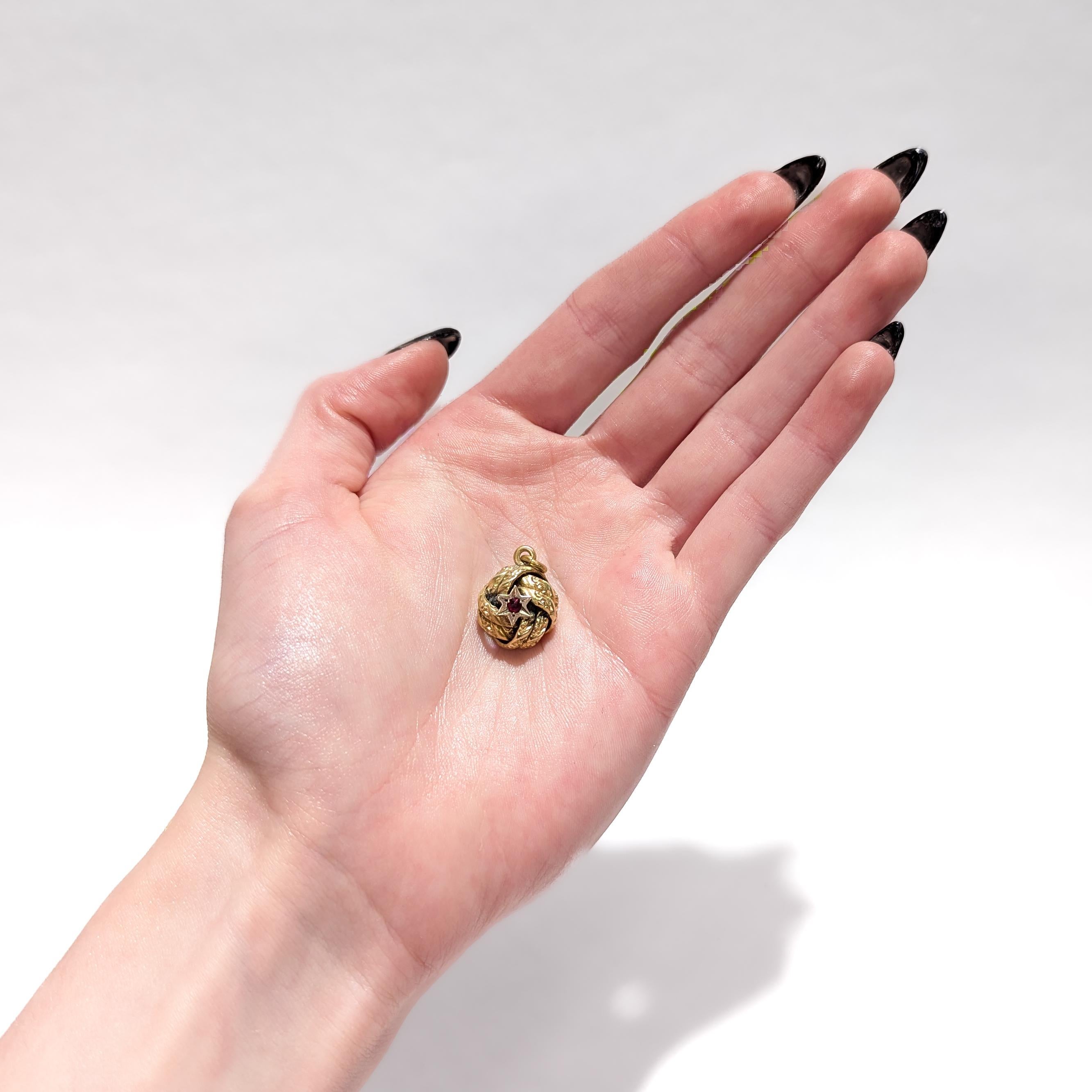 A fine antique gold-filled Aesthetic Movement charm.

With a gold-filled body.

In the form of a love knot. The center of each side with a 6-point star device with a prong-set ruby colored paste cabochon.

Having an integral bail and jump
