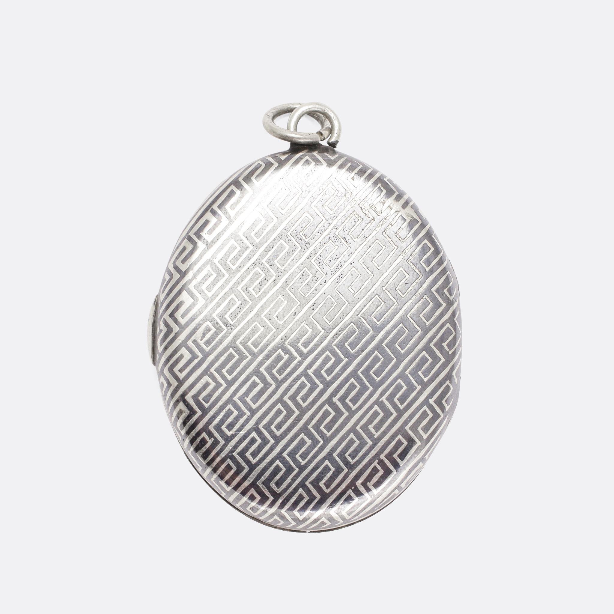 A beautiful, and quite unusual, antique oval locket. The piece is modelled in silver and finished in niello, a blue/black material comprised of copper, lead, silver, and sulphur that, like enamel, is applied to the metal and then fired. The effect