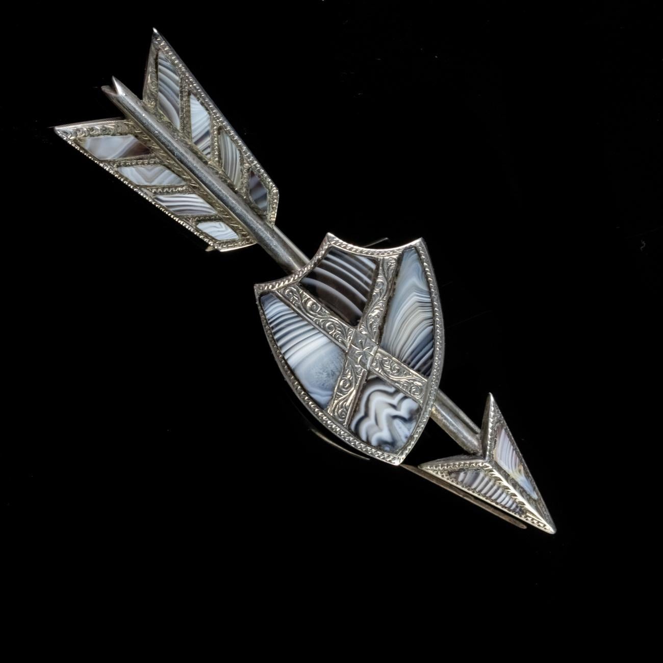 This fantastic Antique Victorian Scottish brooch has been modelled in Silver to form the shape of a shield with an arrow behind it. The silver work features intricate engravings and the brooch has been set with an array of beautiful Montrose Agate