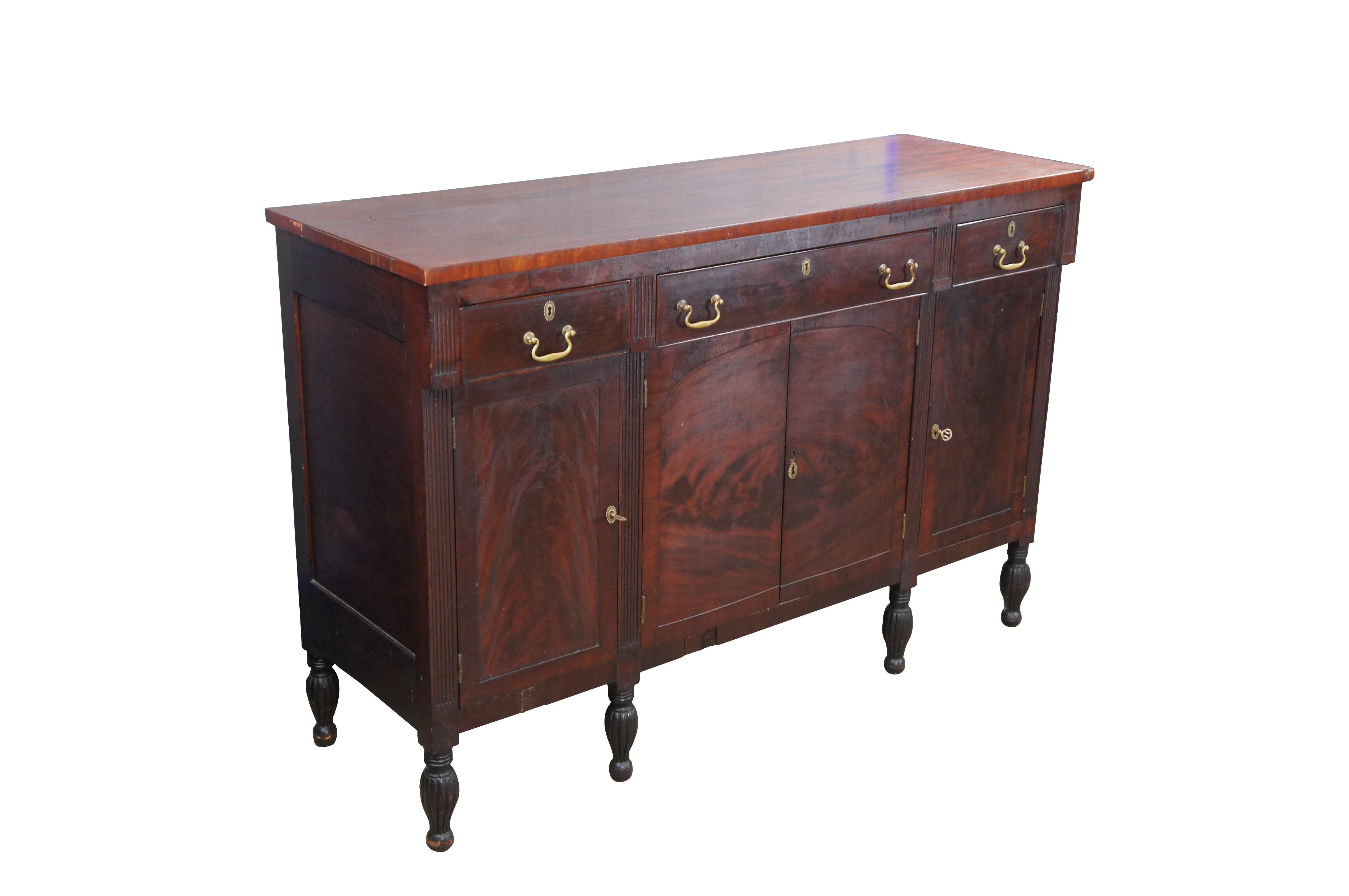 Antique American Empire flame mahogany buffet featuring rectangular form with large central silverware drawer, flanked by drawers over cabinets divided by fluted accents and baluster legs.

Dimensions:
21.5