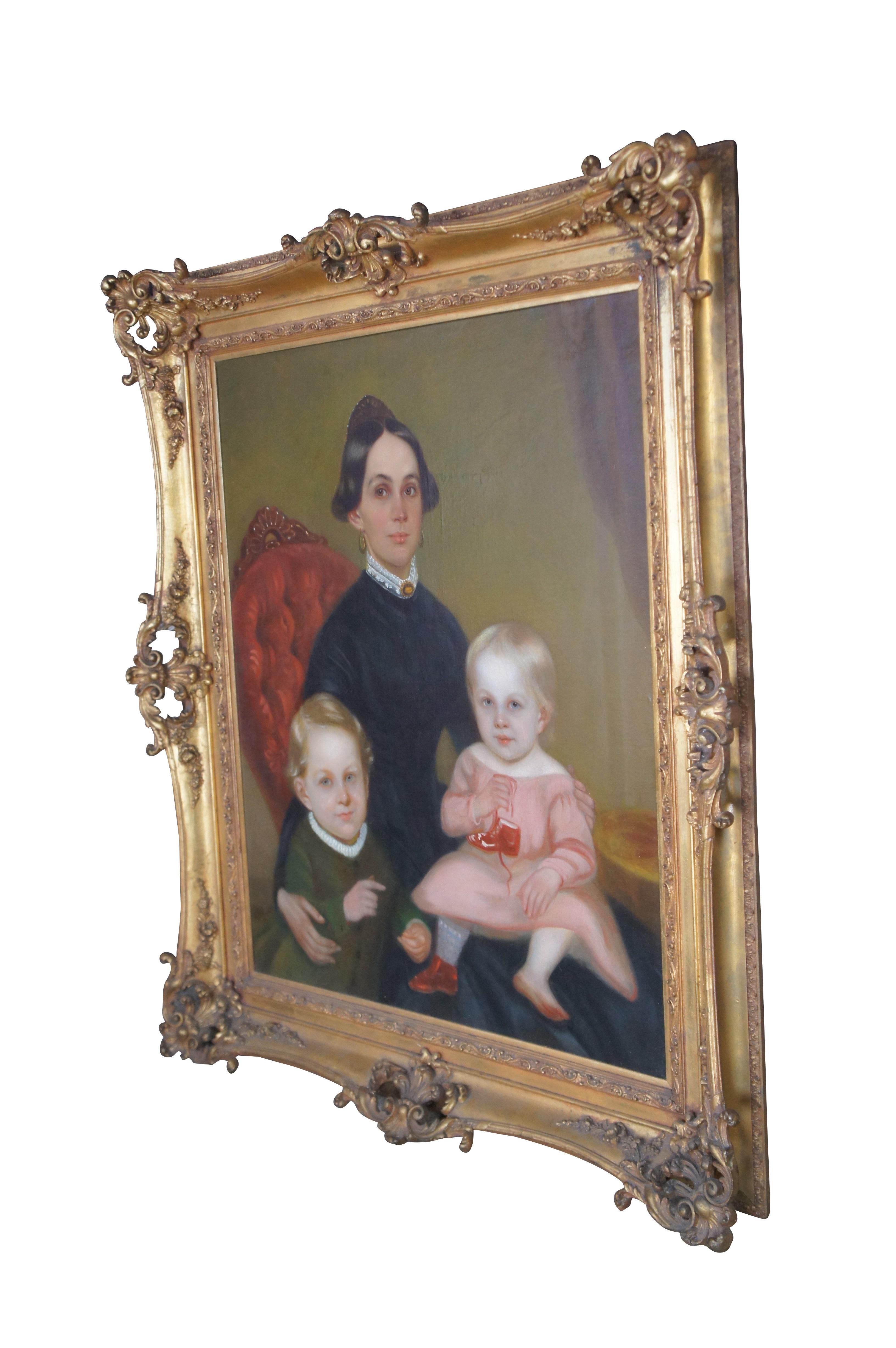 An exceptional large Mid-19th century American School Victorian Folk Art portrait.  The painting features a young, well-dressed mother seated in a tufted balloon-back chair with her children.  The oil painting is ornately framed with pierced foliate