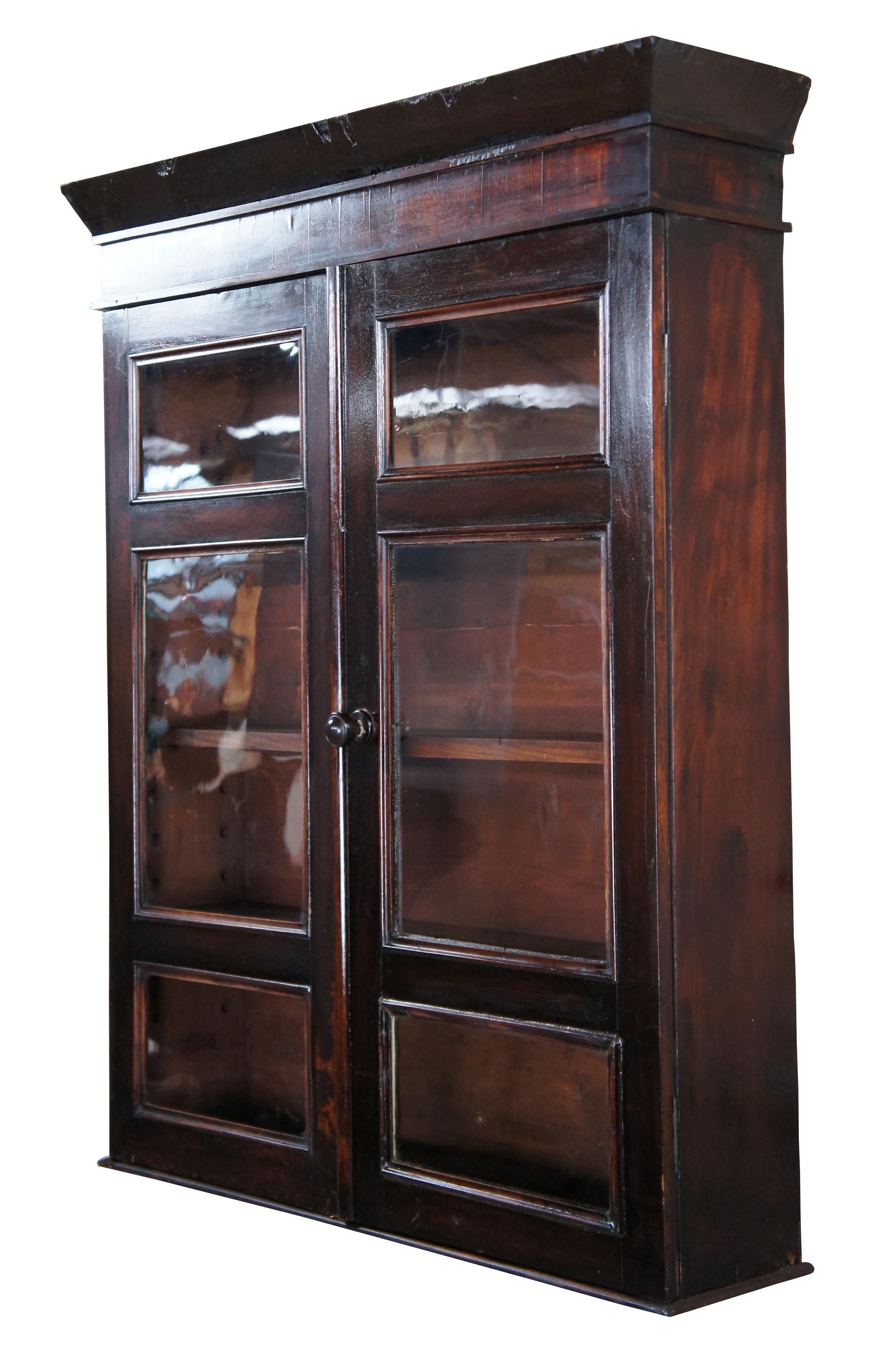 A stunning Victorian era American Country wall hanging curio cabinet Made from mahogany with three adjustable shelves behind original glass paned doors. It's large stature allows for versatile use. A great spice cabinet, hanging cupboard, display