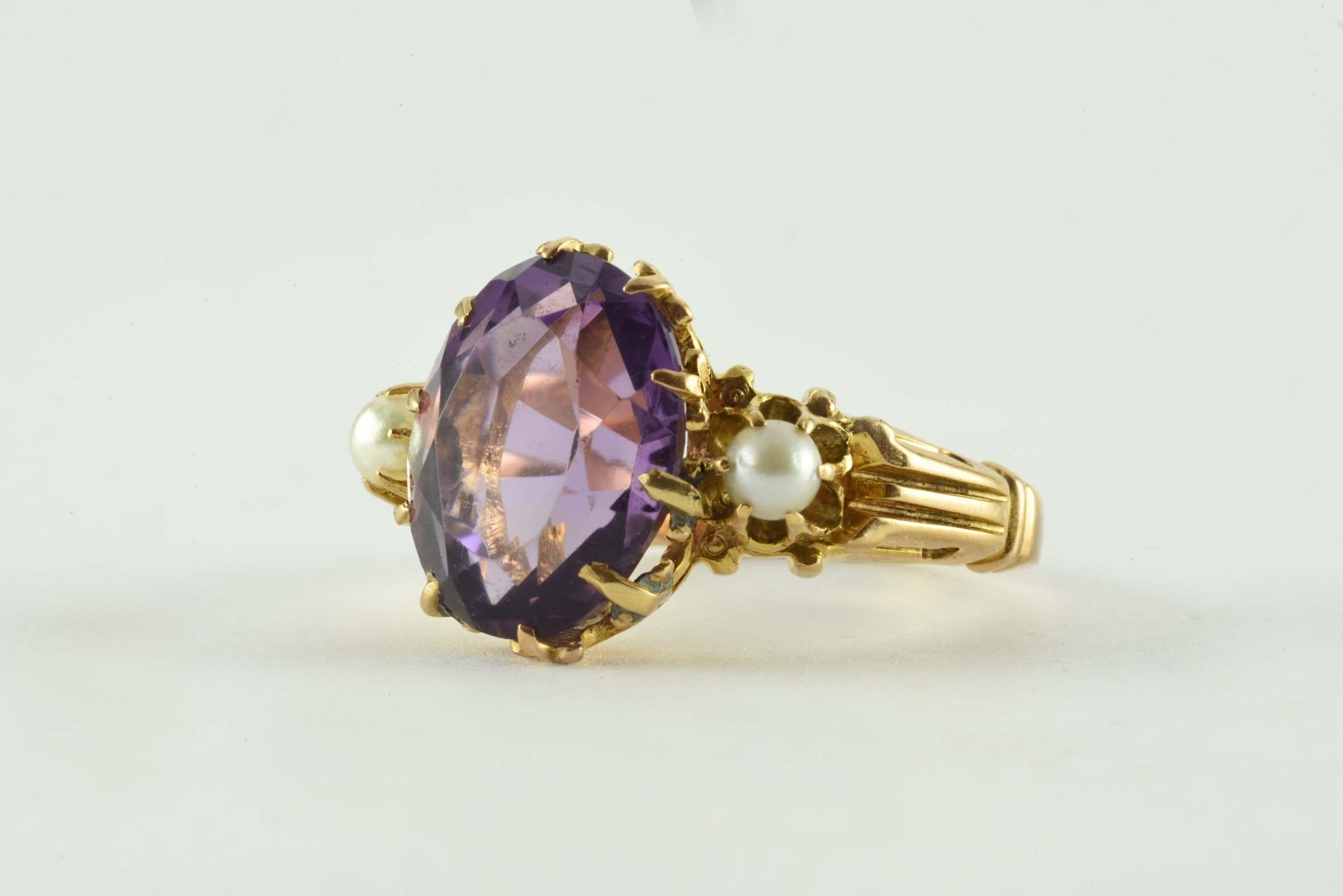 This antique Victorian oval-shaped amethyst center stone measuring 9.7 x 10.11mm is flanked by two 3mm seed pearls and set in 14kt yellow gold. 
