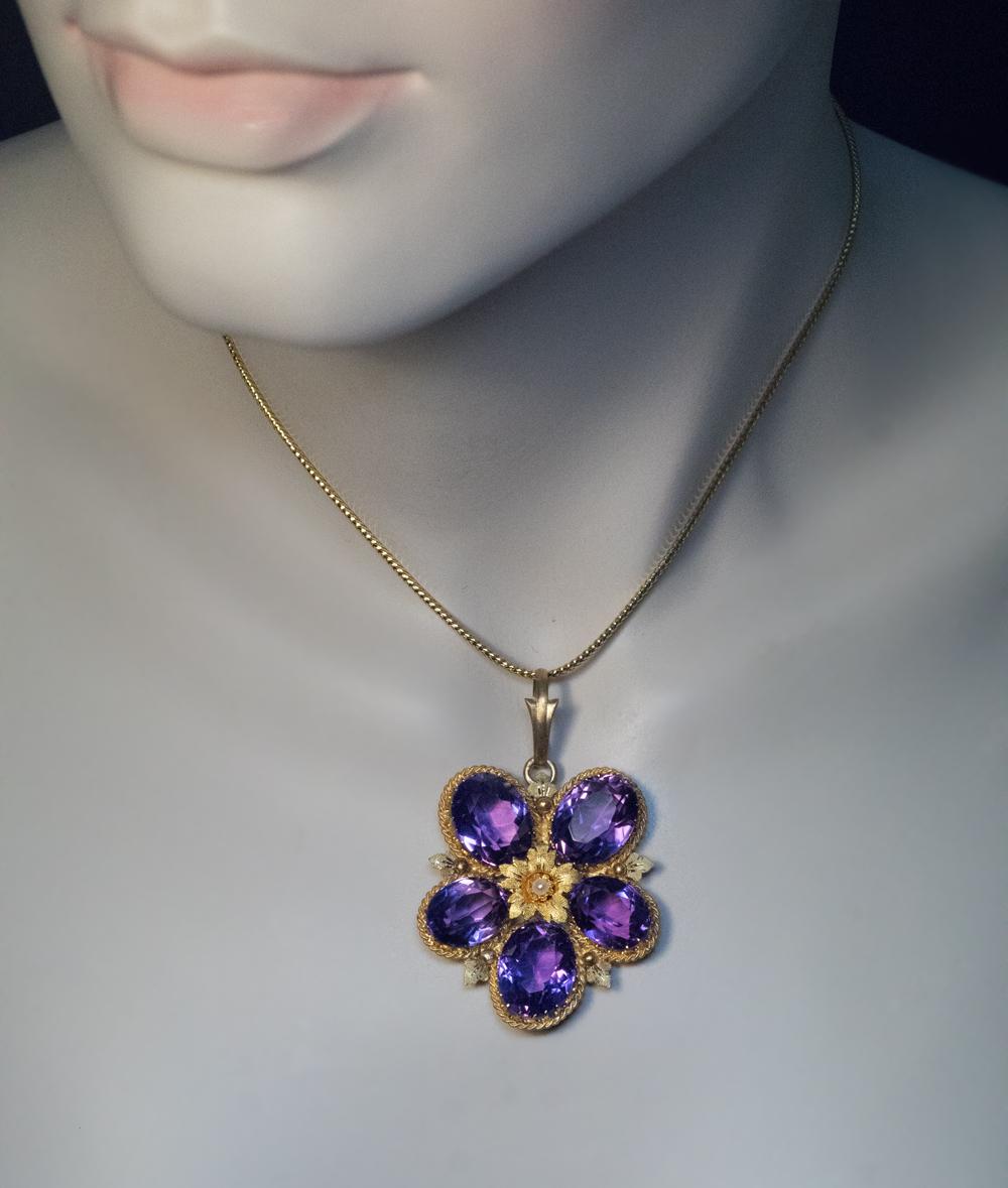 1870s – 1880s

This large 14K yellow gold pendant is designed as a stylized pansy. The leaves are set with five oval amethysts of excellent pinkish purple color. The textured and engraved gold center is accented with a small half pearl.

Marked on