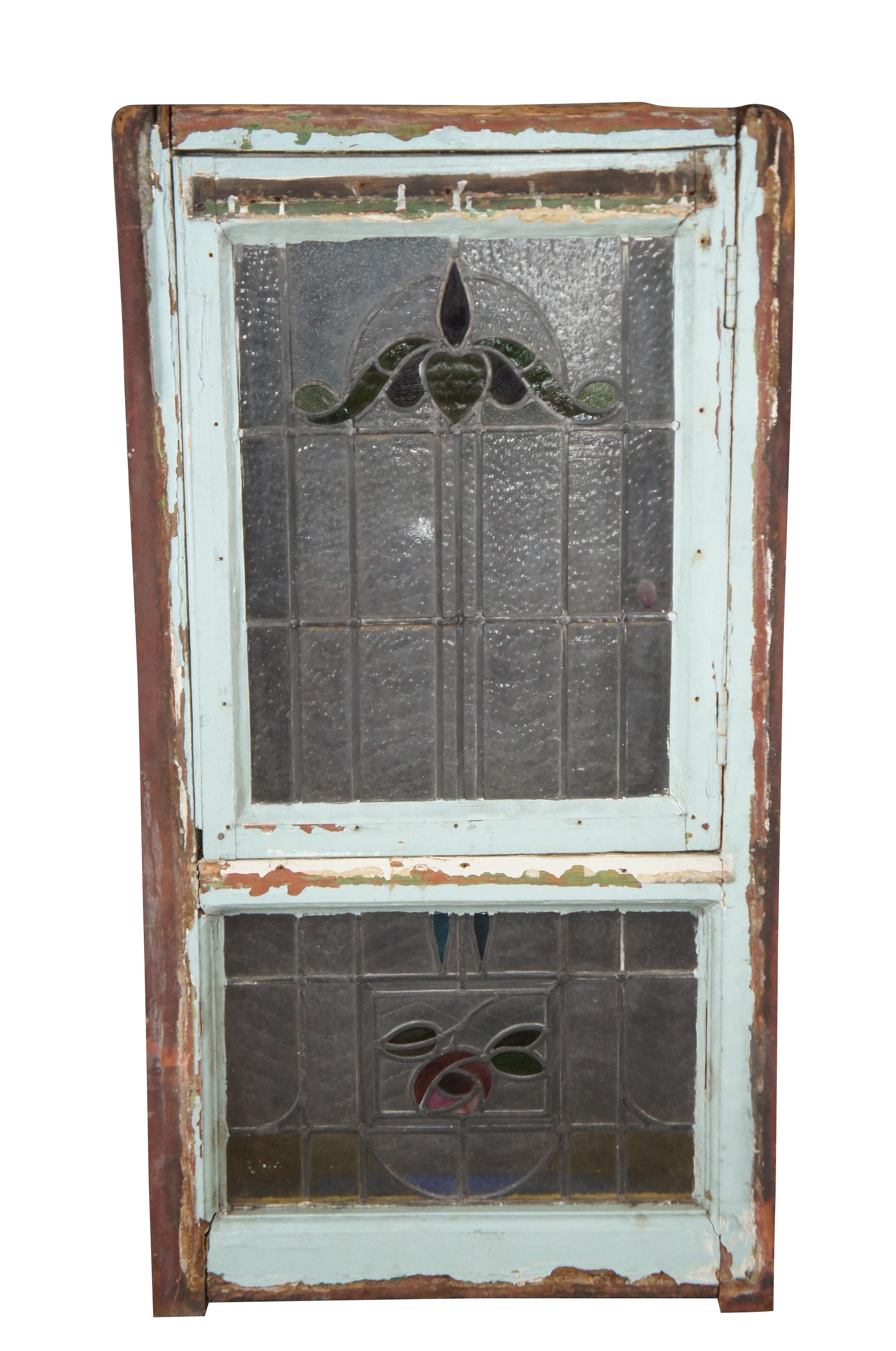 Exquisite reclaimed two part late 19th century leaded stained glass window. Features a large rectangular frame with a large hinged window / door over a transom. Each window is designed with clear, pebbled and textured glass set around ornate floral