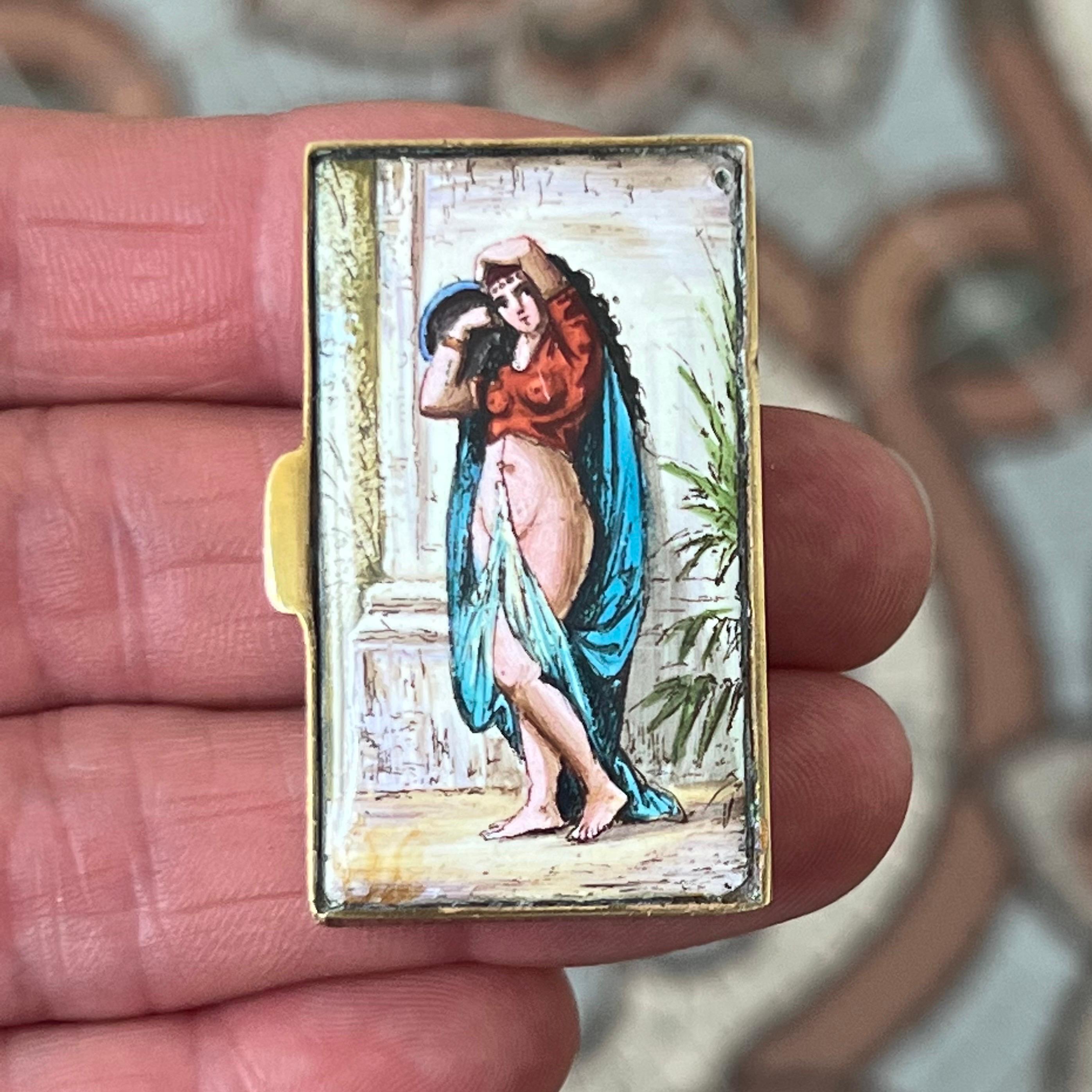 Rare étui à vesta ancien de collection, magnifiquement réalisé en métal doré et décoré d'une plaque d'émail finement peinte. Le recto représente une femme partiellement drapée, probablement une danseuse du ventre, dans des tons vibrants de rouge, de