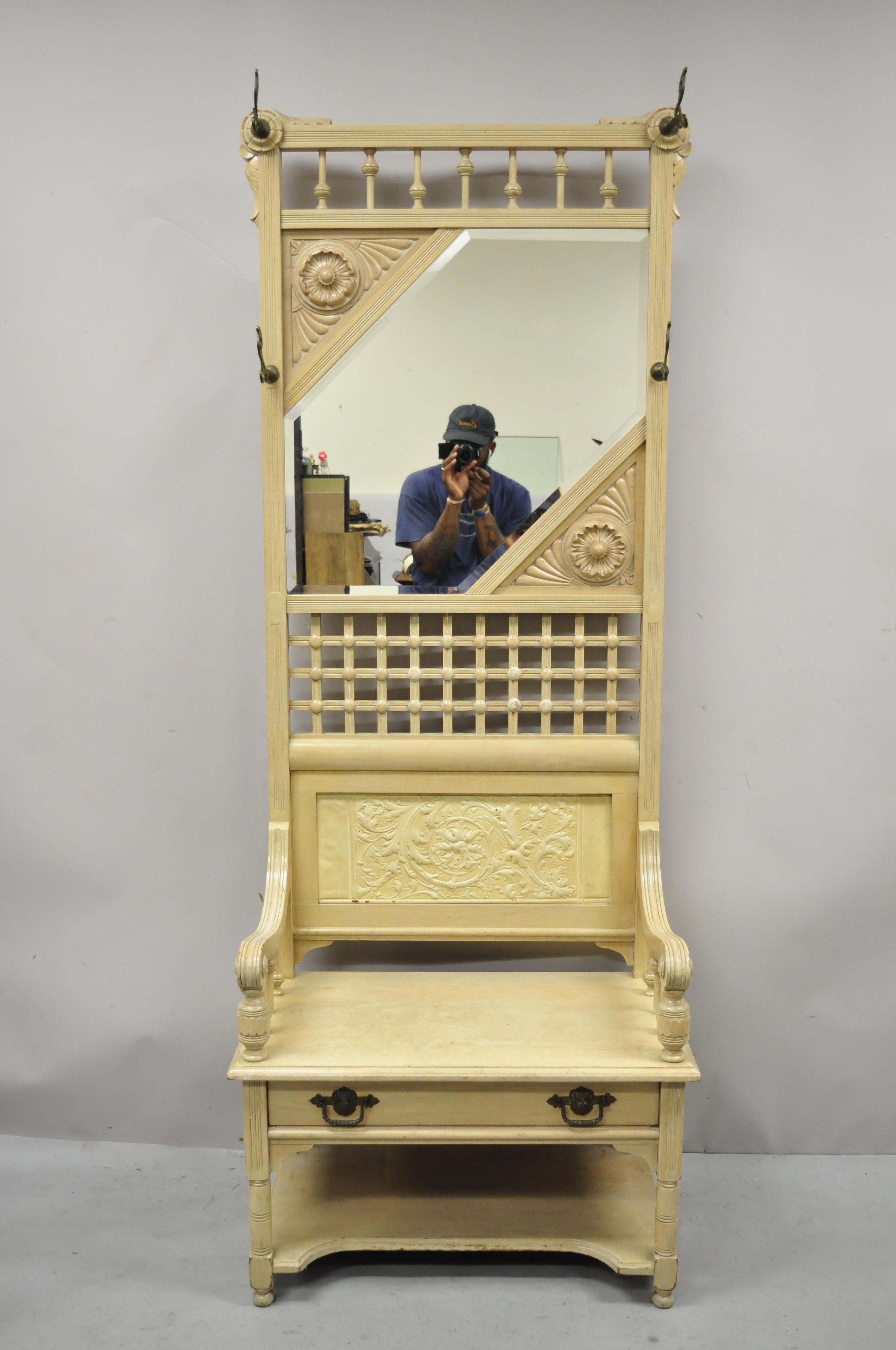 Antique Victorian beveled mirror entry hall coat tree with bench seat and drawer. Item features beveled glass mirror, stick and ball spindle carvings, 4 brass coat hooks, leafy scrollwork carved back panel, seat with arms and lower drawer, solid