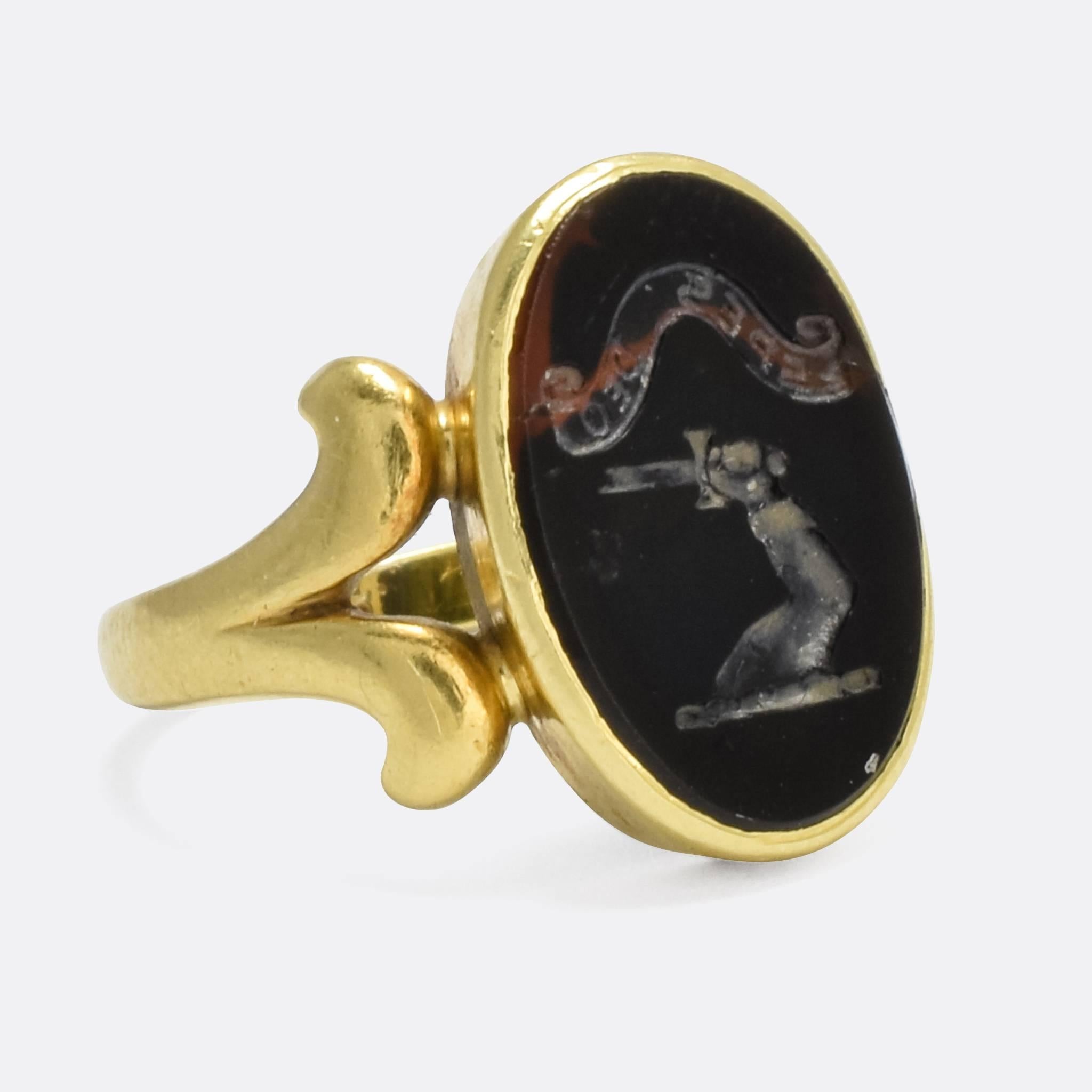 A cool antique signet ring with an intaglio bloodstone panel. The oval stone is carved with an English heraldic crest and motto: an arm upstretched holding a broken sword, beneath the words 