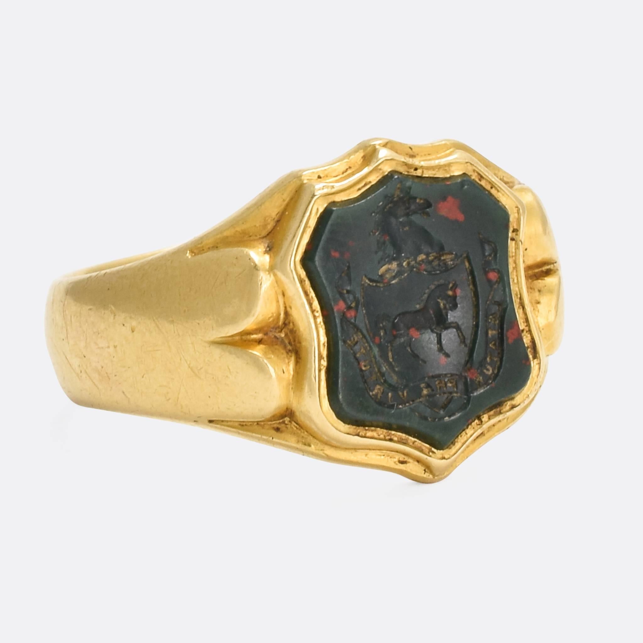 A fine antique signet ring set with a shield-shaped bloodstone panel carved with a heraldic intaglio crest and Latin motto. The motto reads 
