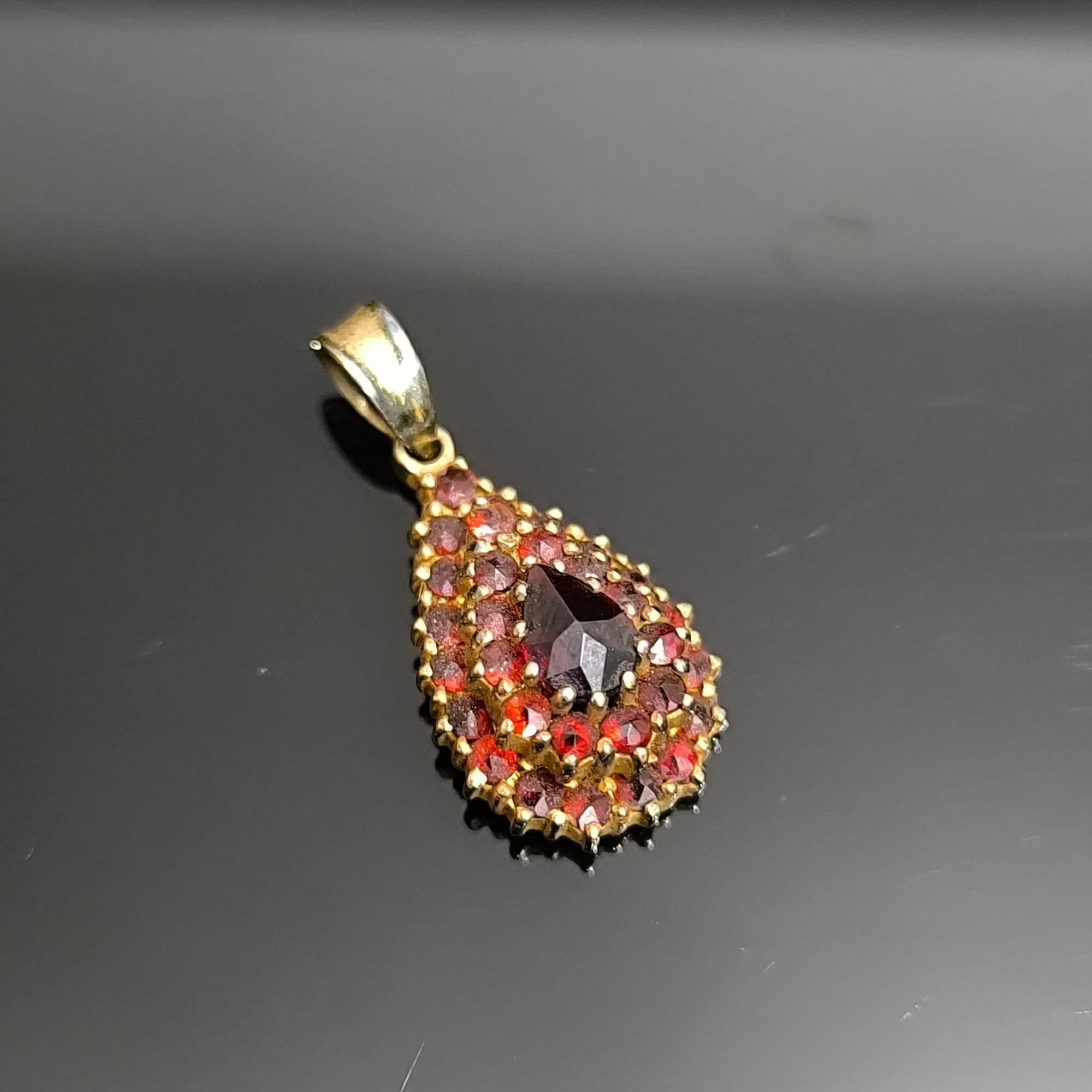 Questo ciondolo vintage con granato, ricco di dettagli, presenta una silhouette a goccia a due livelli incastonata in argento 925 placcato oro, con marchio di purezza sterlina. I granati rosso intenso sono disposti in strati concentrici, creando un