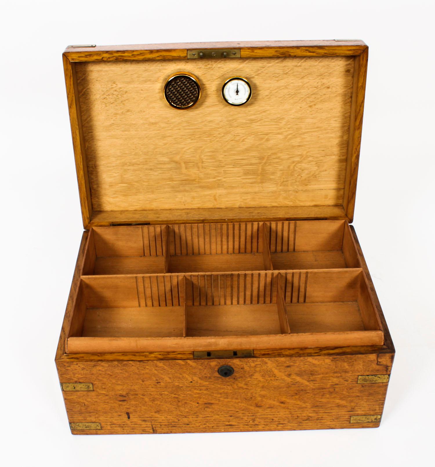 This is a stylish antique Victorian oak brass and cedar lined tabletop cigar humidor circa 1860 in date.

The rectangular box features a lift out tray and adjustable divisions with sunken handles to the sides and a hinged lid with a central brass