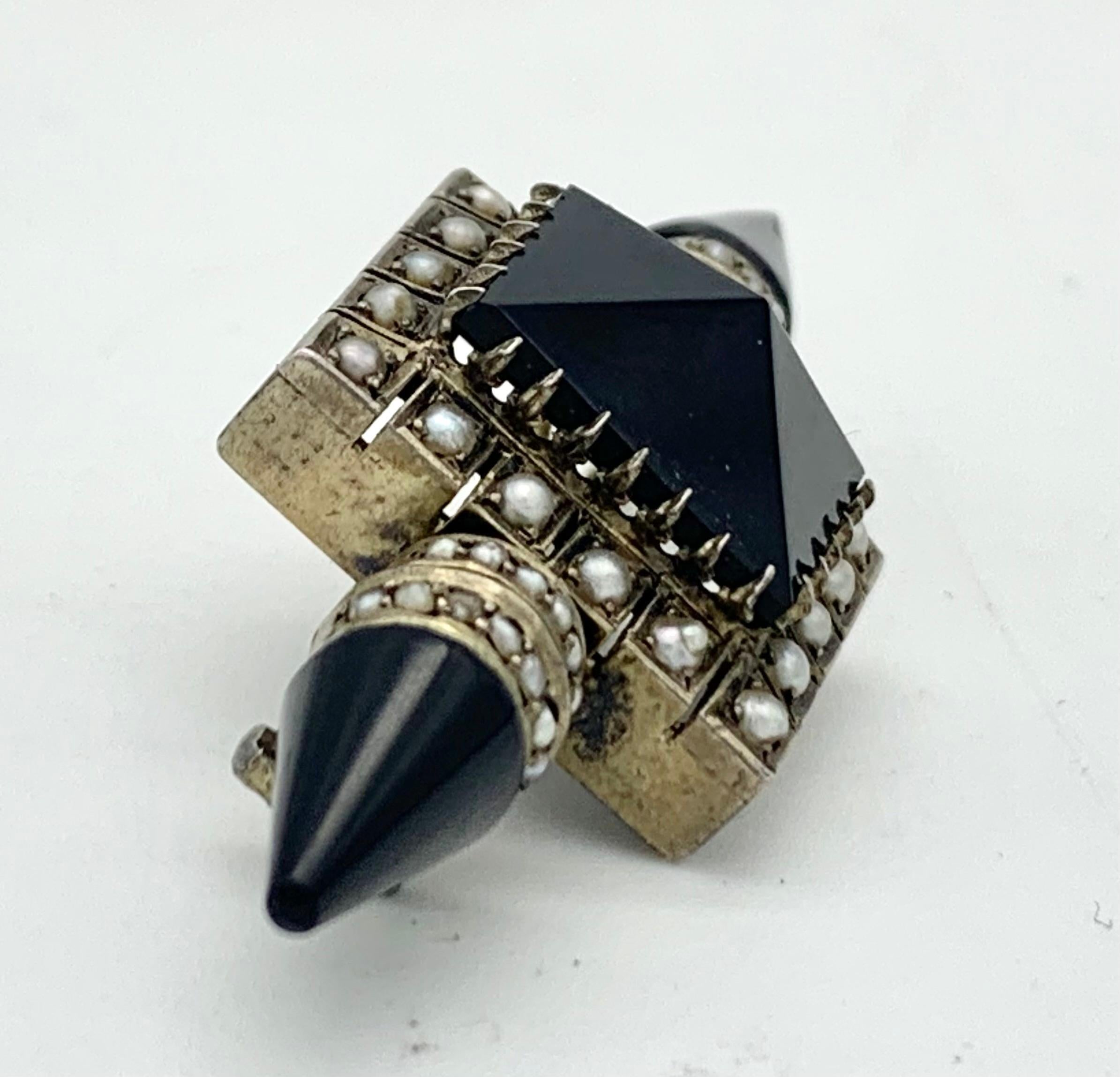 The brooch was handcrafted in 1880 ca. In the center of this extravagant piece of jeweller we see a large rectangular pyramid shaped onyx in a claw set frame set with eighteen seed pearls.  Two conical cut pieces of onyx are mounted on circular
