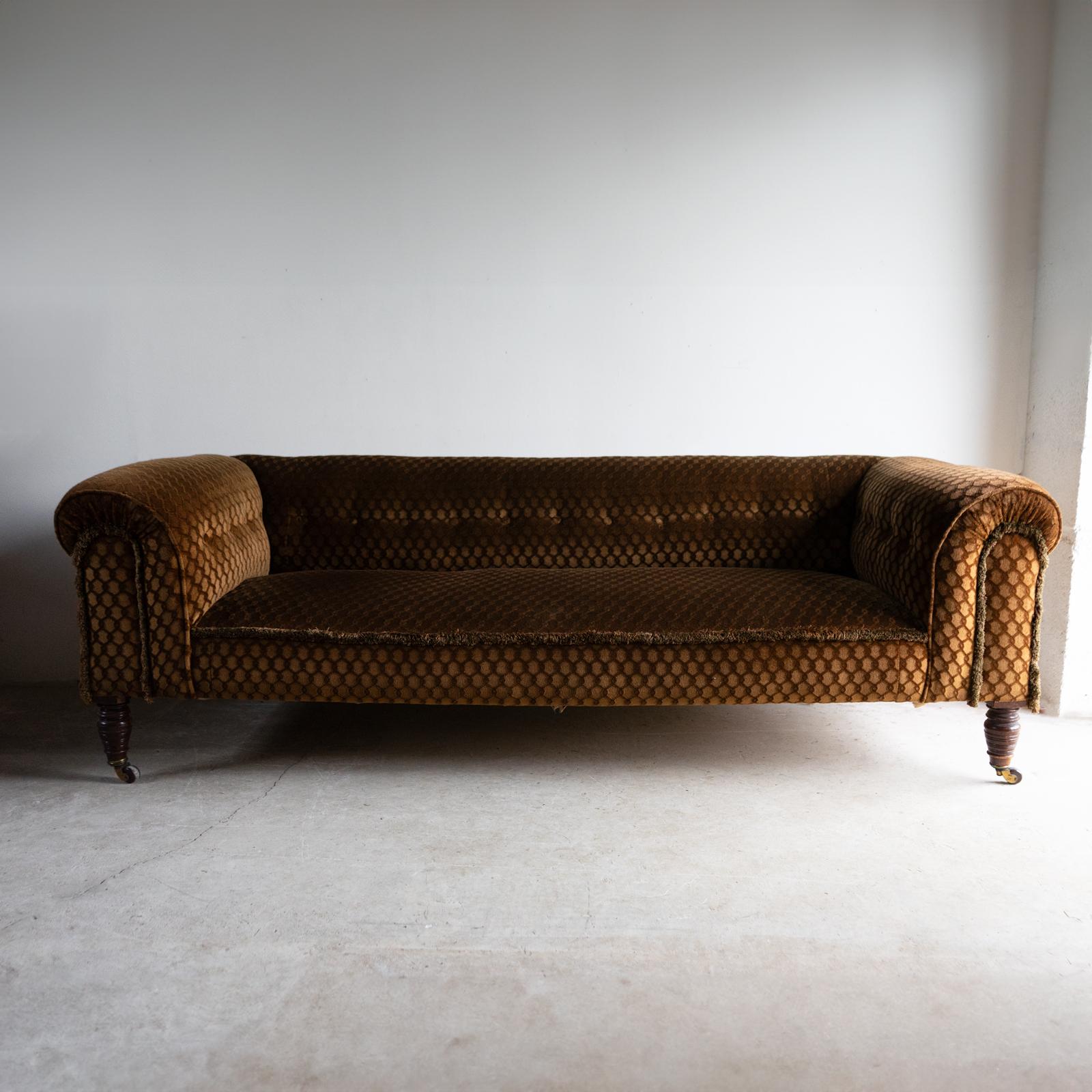 ANTIQUE THEE SEATER SETTEE, LATE 19TH CENTURY 

Sumptuous, button-backed sofa with brown/gold velvet upholstery with geometric pattern design and fringed details.

Raised on turned legs with its original brass and ceramic castors. 

It is in very