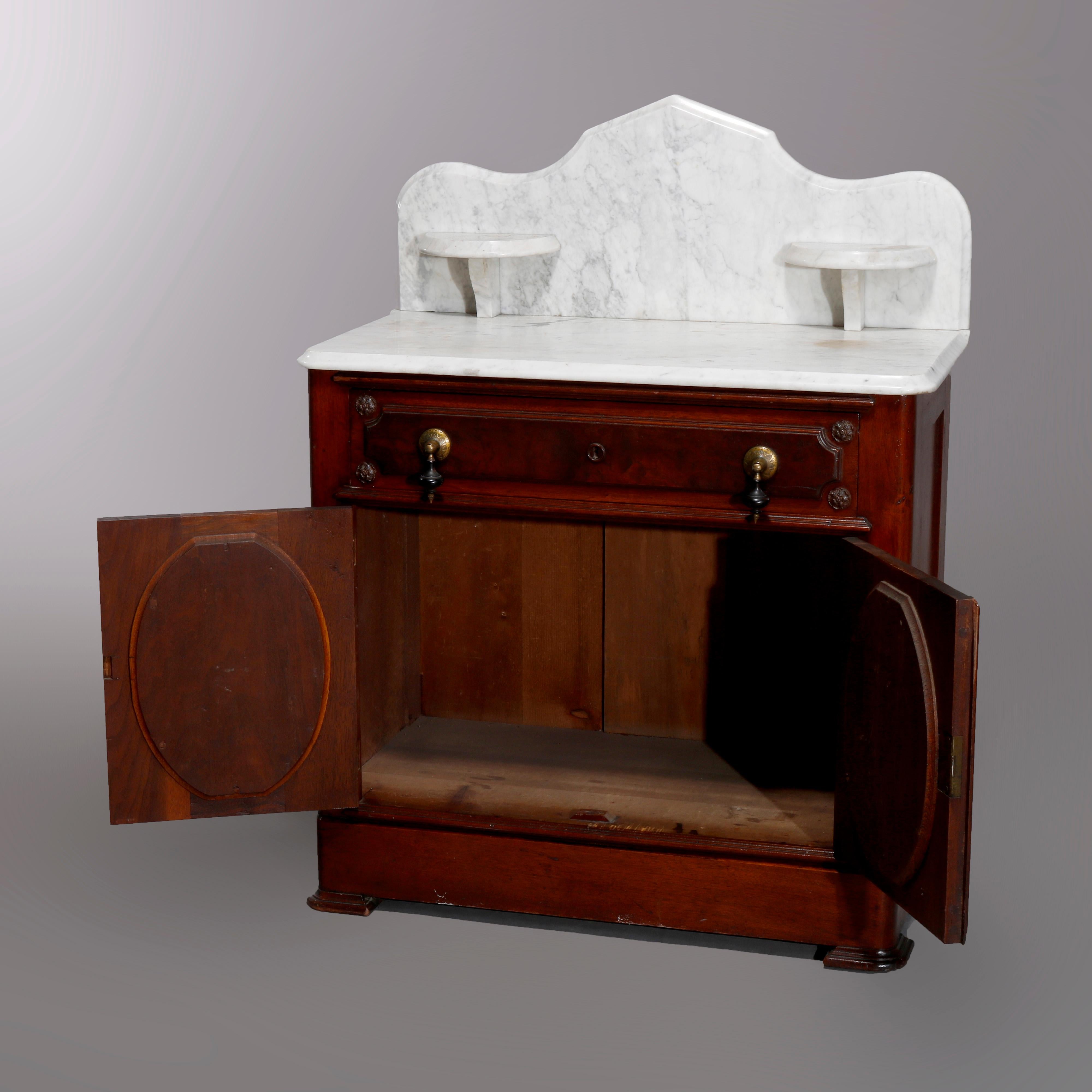 An antique Victorian washstand offers marble top having shaped backsplash with flanking candle stands and surmounting walnut base with burl frieze drawer over double paneled door cabinet, c1890

Measures: 40.75