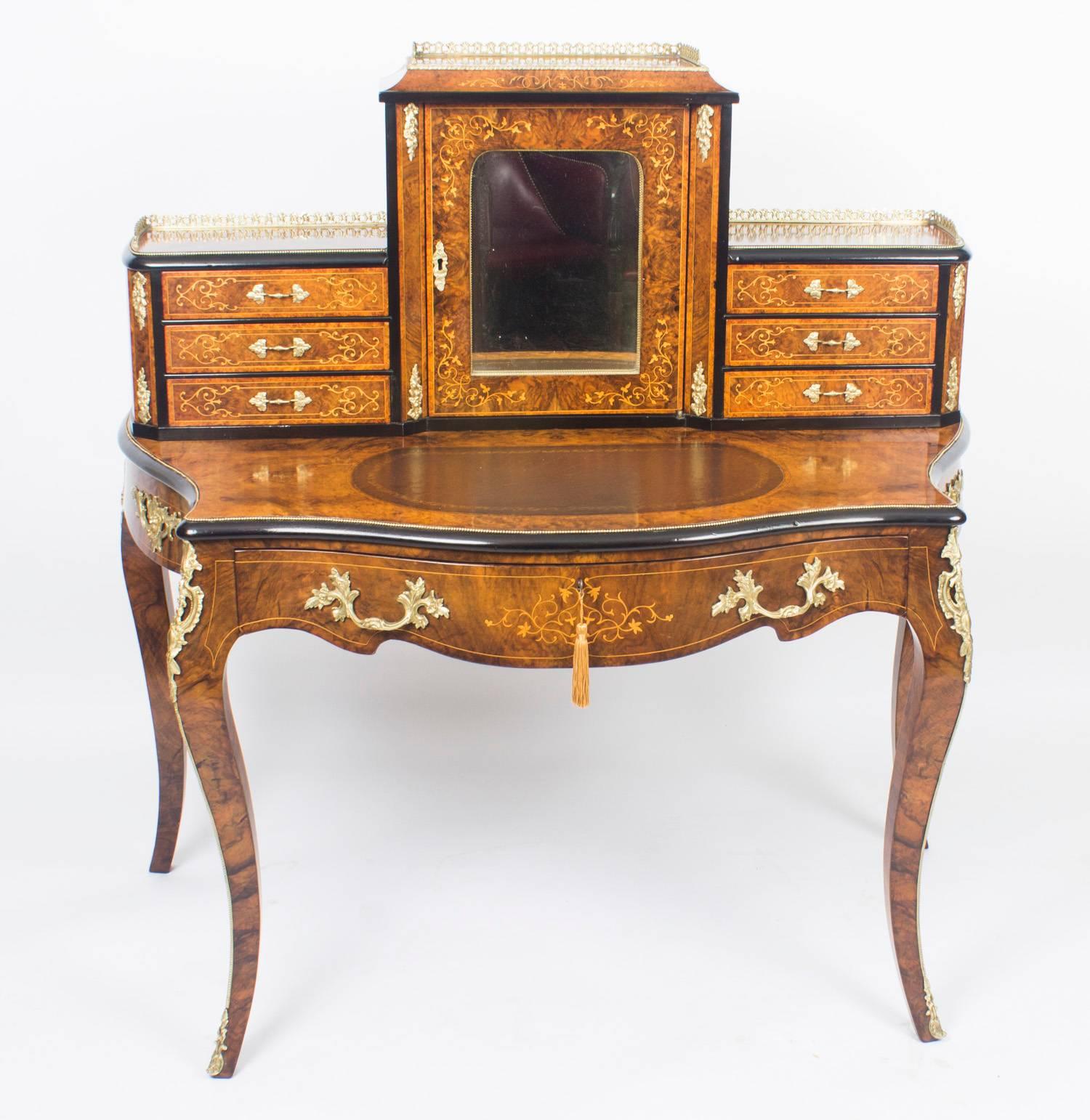 This is a gorgeous Victorian burr walnut and marquetry Bonheur Du Jour, or Ladies writing desk, circa 1860 in date. 

The superstructure comprises a large central bay with a mirror inset door and a three quarter brass gallery above. The door opens