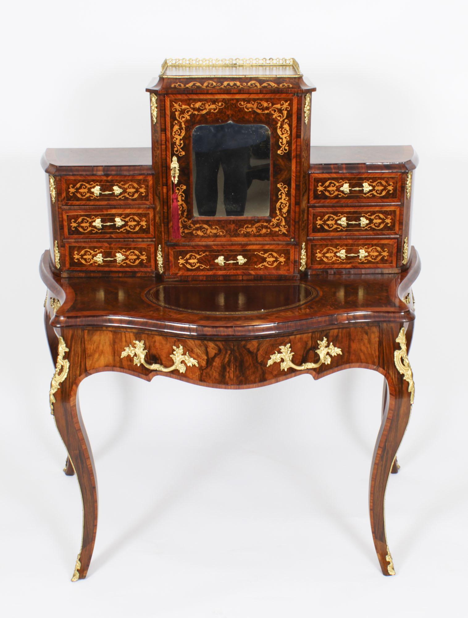 This is a elegant Victorian burr walnut and marquetry Bonheur Du Jour, or Ladies writing desk, circa 1860 in date. 
 
The superstructure comprises a large central bay with a mirror inset door and a three quarter brass gallery above. The door opens